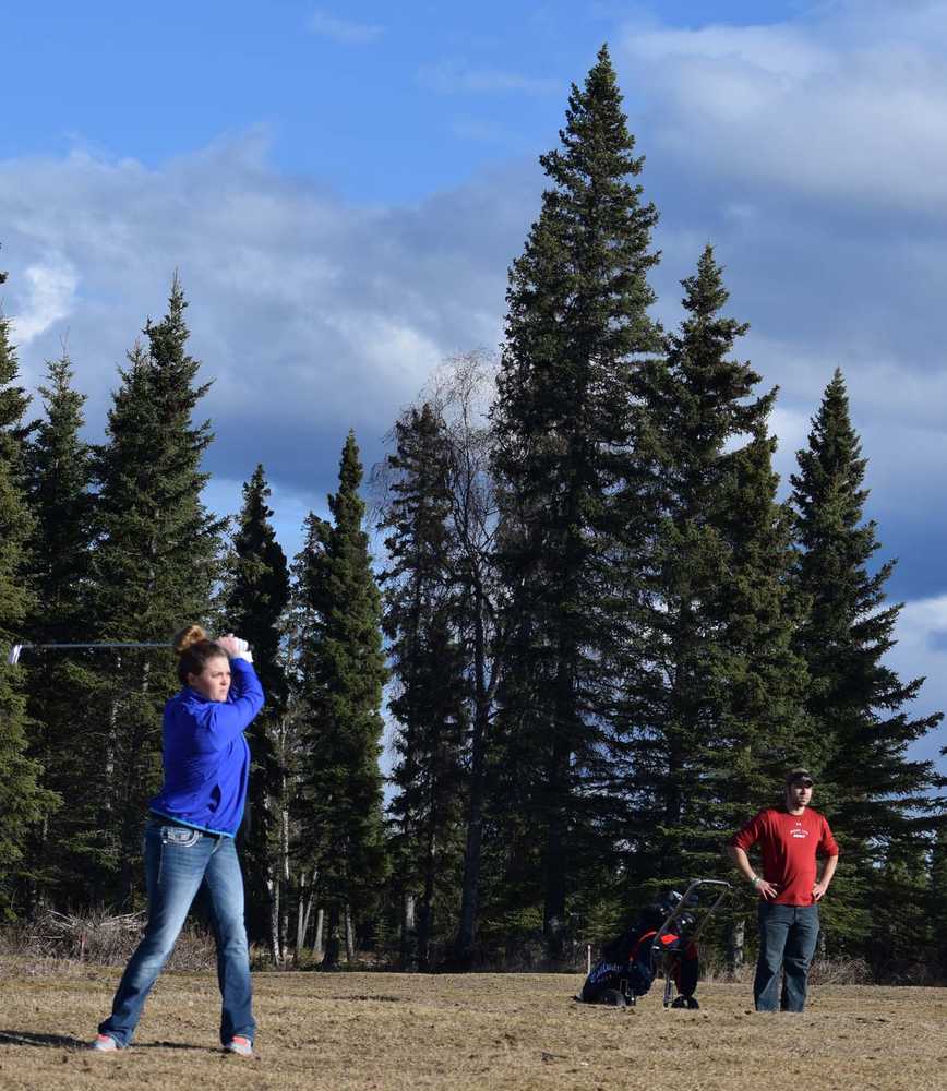 Photo by Jeff Helminiak/Peninsula Clarion Molly Streich, of Kenai, hits an approach shot to the eighth green at Kenai Golf Course on Sunday as Billy Anderson, of Nikiski, observes. When Streich asked Anderson if he wanted to golf Sunday, Anderson didn't believe the course was open. The course opened Tuesday, the earliest opening ever.