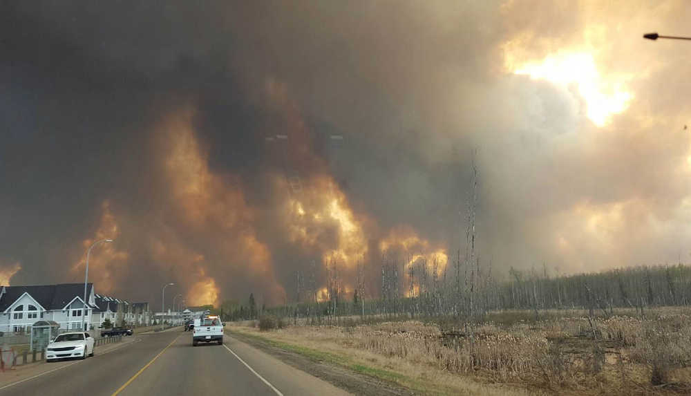 This photo take through a car windshield shows smoke rising from a wildfire rages outside of Fort McMurray, Alberta, Tuesday, May 3, 2016. The entire population of the Canadian oil sands city of Fort McMurray, has been ordered to evacuate as a wildfire whipped by winds engulfed homes and sent ash raining down on residents. (Mary Anne Sexsmith-Segato/The Canadian Press via AP) MANDATORY CREDIT