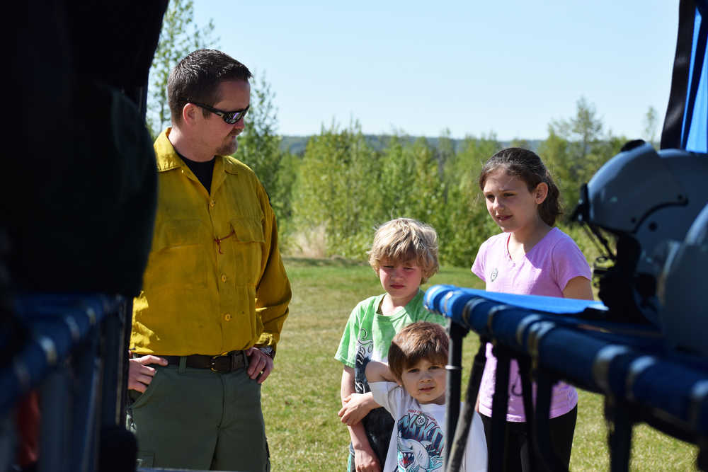 Photo by Megan Pacer/Peninsula Clarion Wildland Fire and Resource Technician 3 Nick Adamson explains the ins and outs of a Bell 212 "Huey" helicopter to 3-year-old Casey Dahlman, 8-year-old Spencer Dahlman and 11-year-old Ashley Dahlman during an Alaska Division of Forestry open house Saturday, May 14, 2016 at the Kenai-Kodiak Area Office in Soldotna, Alaska.