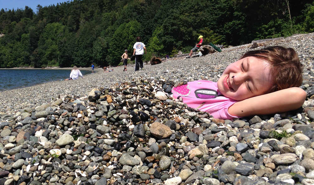 ADVANCE FOR WEEKEND EDITIONS - In this June 2, 2016 photo, Hazel Loerch rests on the beach at Cama Beach State Park, buried under the excellent rocks. (Jessi Loerch/The Herald via AP) MANDATORY CREDIT