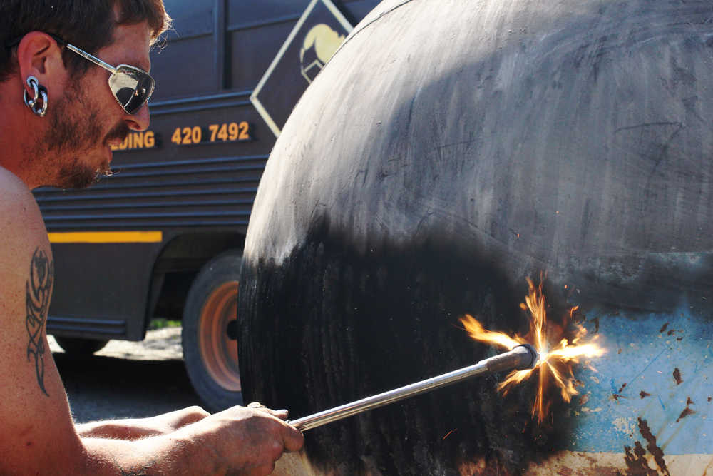 Ben Boettger/Peinsula Clarion RAW welder Laron Hagan burns paint off a buoy, preparing to plasma-cut the steel surface with a scene of dragons and skeletons on Monday, July 18 at the RAW Welding workshop outside Soldotna.