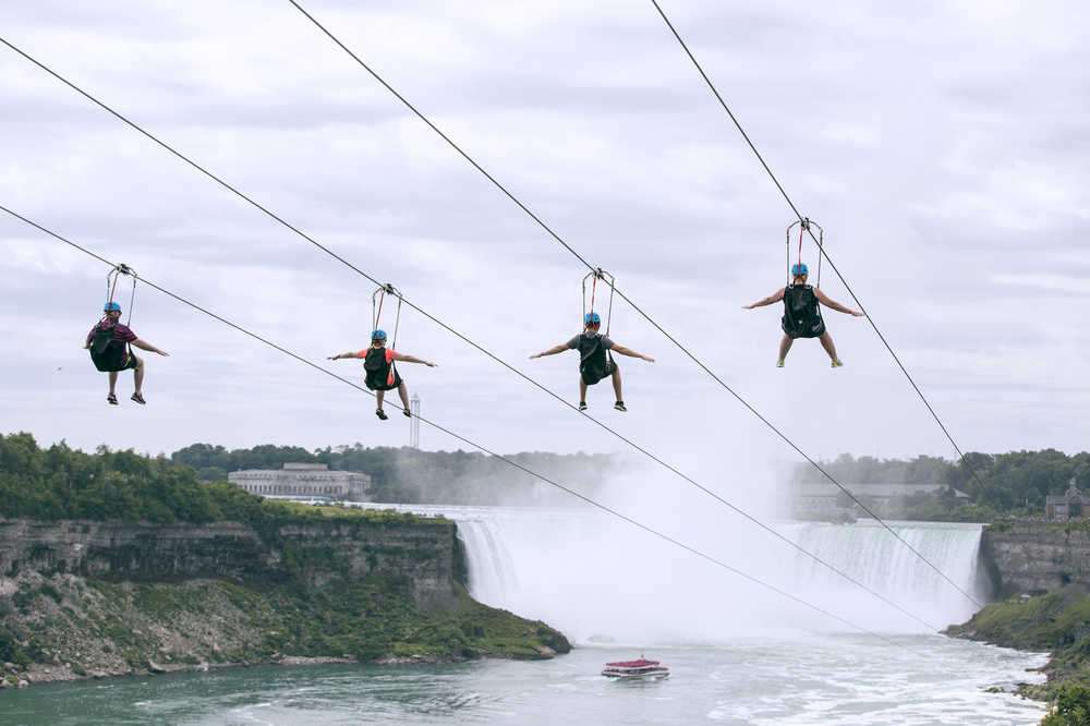 In this July 19, 2016 photo provided by WildPlay Ltd., tourists suspended above the water from zip lines make their way at speeds of up to 40 mph toward the the mist of the Horseshoe Falls, on the Ontario side of Niagara Falls. The overhead cables have evolved from a fun way to explore jungle canopies to trendy additions for long-established outdoor destinations. (Kien Tran/WildPlay Ltd. via AP)
