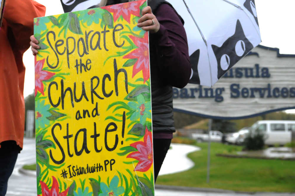 Photo by Elizabeth Earl/Peninsula Clarion Kyra Bodnar holds a hand-painted sign near where members of the Catholic Church gathered to pray near the Kenai Peninsula Borough Administration Building on Wednesday, Aug. 17, 2016 in Soldotna, Alaska. The church members decided to pray outside the borough administration building after a Satanic invocation was given to open the borough assembly meeting Aug. 9.