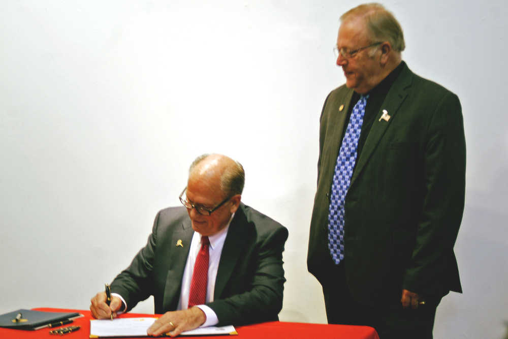 Photo by Elizabeth Earl/Peninsula Clarion Gov. Bill Walker (left) signs HB 100 into law as Speaker of the Alaska House of Representatives Mike Chenault (right) watches Monday, Sept. 12, 2016 in Kenai, Alaska. Walker visited the central Kenai Peninsula Monday to give a speech at a joint Kenai and Soldotna chambers of commerce luncheon and to participate in a worksession with the Kenai Peninsula Borough Assembly.