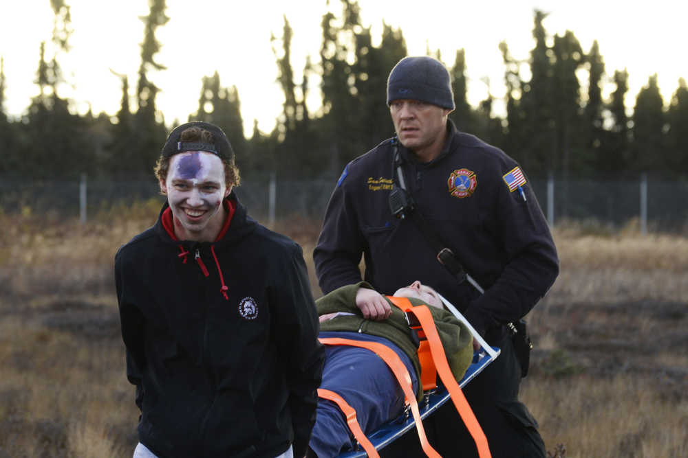 Photo by Megan Pacer/Peninsula Clarion Evan Butcher, a member of the Kenai River Brown Bears hockey team, helps a Kenai firefighter carry a volunteer victim on a stretcher to safety during a mass casualty drill Tuesday, Oct. 11, 2016 at the Kenai Municipal Airport in Kenai, Alaska. The airport is required by the Federal Aviation Administration to hold the drill every three years to test its emergency planning.