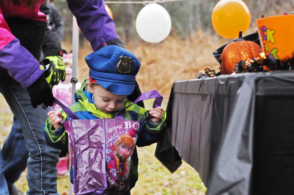 Photo by Elizabeth Earl/Peninsula Clarion Karbon Lindley, 18 months, dressed up as an Alaska State Trooper, sneaks a look at his candy stash on a walk through the trails system during the annual Tsalteshi Trails Spook Night on Sunday, Oct. 30, 2016 in Soldotna, Alaska. Families walked through the trail system and visited at stations sponsored by local businesses, government agencies and political candidates, collecting every kind of goodie from candy to keychains to reflective shoelaces - handed out by the City of Soldotna - just before a group of runners took off into the trails for a 5K.