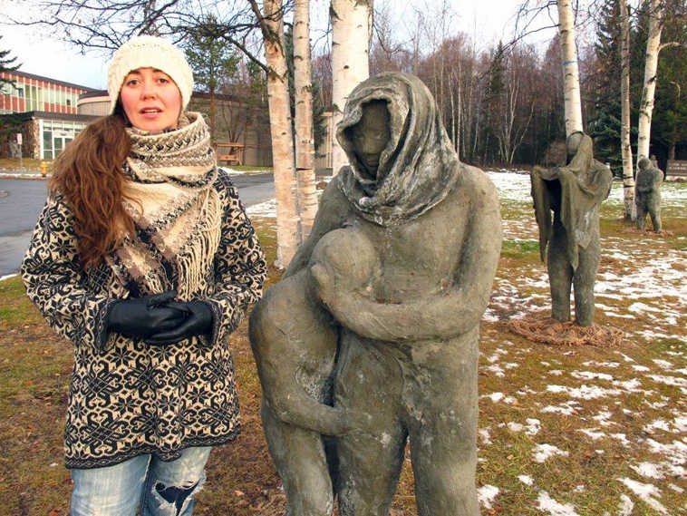 Artist Sarah Davies stands near statues in a new public art installation Wednesday, Nov. 2, 2016, at Alaska Pacific University in Anchorage, Alaska. Davies was also the lead artist in an art installation that included the sculptures, which have been restored for the exhibit opening Friday after they were damaged by tides and high winds last year. (AP Photo/Rachel D'Oro)