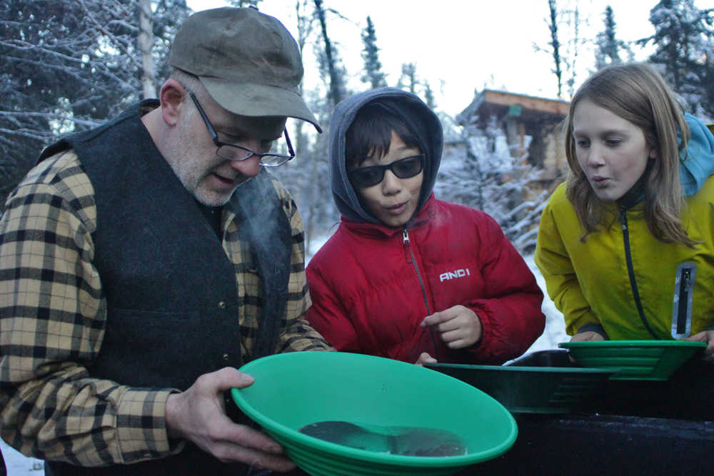 Ben Boettger/Peninsula Clarion Prospector Steve Morris (left) taps a pan of water and concentrated sediment, which he dredged from a nearby river, to reveal gold flakes to onlooking Seward Elementary students Bengimiin Ambrosiani and Aloshia Cross during a fieldtrip to Manitoba Cabin on Tuesday, Nov. 15, near the Seward Highway.