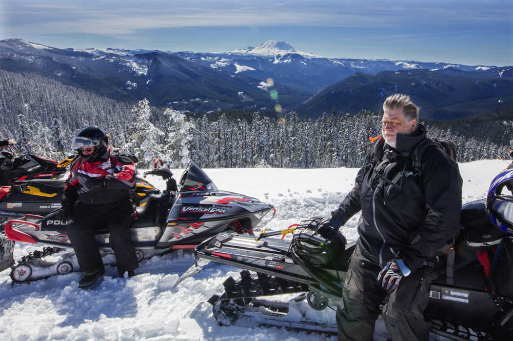 In this Tuesday, March 17, 2016 photo, Bob Seelye and Mick Steinman sit on their snowmobiles on the very top viewpoint of the trail system near Crystal Springs Sno-Park in Wash. Mount Rainier in the distance.  (Steve Ringman/The Seattle Times via AP)