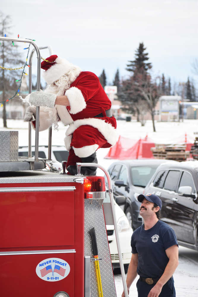 Photo by Megan Pacer/Peninsula Clarion Santa climbs down from a Kenai Fire Department engine to greet families and children gathered Friday, Nov. 25, 2016 at the Kenai Chamber of Commerce and Visitor Center in Kenai, Alaska. Some visitors lined up more than an hour before Santa arrived to take part in the annual tradition.