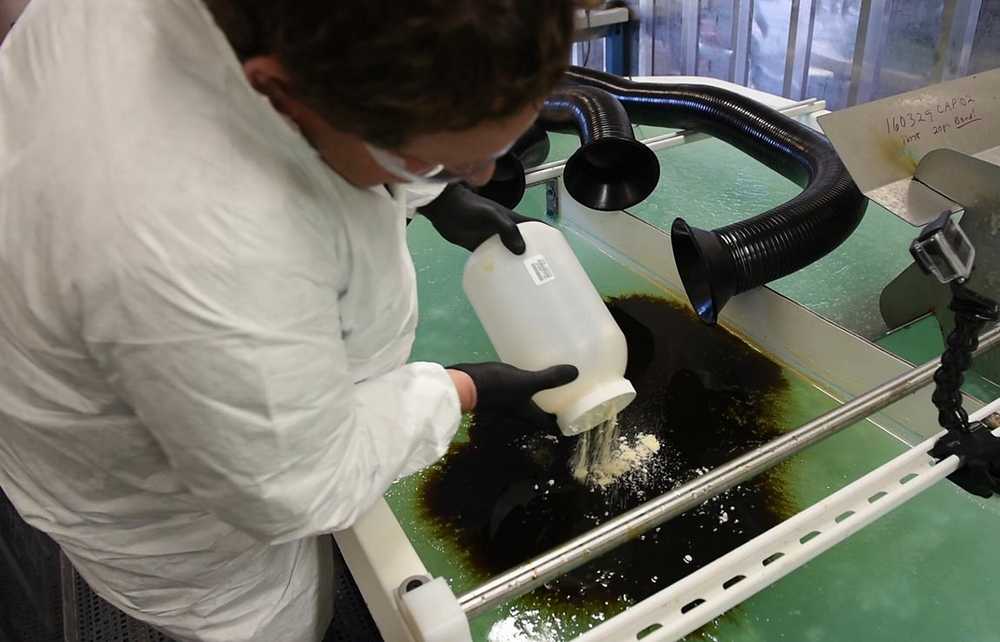 In this Dec. 9, 2016  photo, courtesy of Pacific Northwest National Laboratory, PNNL microbiologist Robert Jeters sprinkles PNNL's chemically modified sawdust onto a small oil spill inside the Arctic simulation lab, where researchers mimic extreme freezing conditions and make icy slush that is similar to what is found on the surface of the Arctic Sea during a demonstration of sawdust oil recovery material research at the PNNL in Richland, Wash. (Pacific Northwest National Laboratory via AP)