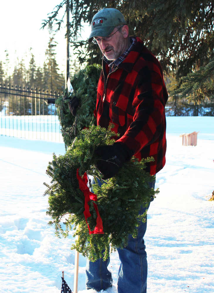 Photo by Megan Pacer/Peninsula Clarion Jim Halliday of Nikiski hangs a wreath on a steak marking the grave of a veteran Saturday, Dec. 17, 2016 at the Kenai Municipal Cemetery in Kenai, Alaska. Bob Myles, a member of the VFW and American Legion, coordinated the peninsula's first wreath ceremony through the Wreaths Across America program. Community members hung wreaths on the graves of veterans in the Kenai and Soldotna cemeteries, and Myles is working to expand the event to more peninsula cemeteries next year.