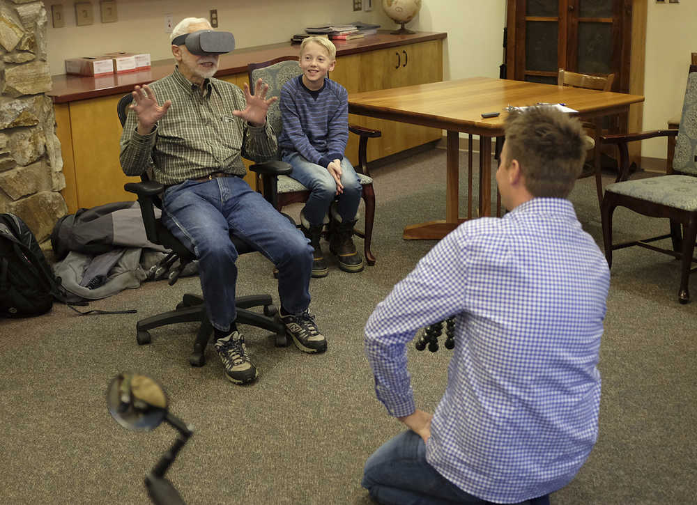 ADVANCE FOR SATURDAY DEC. 24, 2016 AND THEREAFTER - In this Dec. 13, 2016 photo, Pioneers Home resident Joe Nistler, 90, reacts to a virtual reality video of a herd of elephants walking while Lincoln Markham, right, watches in Fairbanks, Alaska. Lincoln Markham and Dan Markham are the father-son duo behind the extremely popular What's Inside YouTube channel. (Matt Buxton/Fairbanks Daily News-Miner via AP)