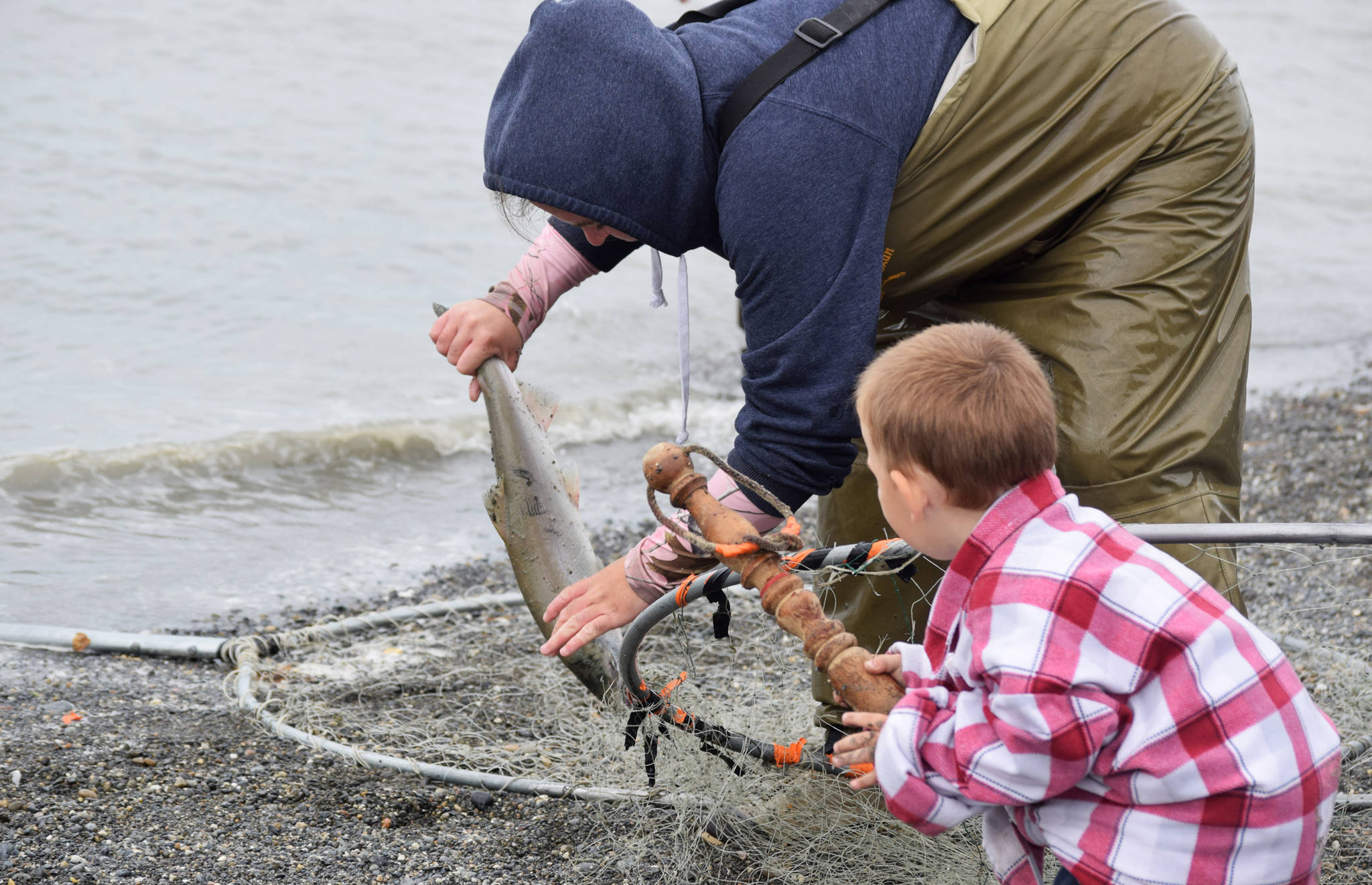 Onya Pate (left) of Soldotna lifts a sockeye salmon she caught in the Kasilof River from her dipnet while her son Epic Lee (right) hands her a bonker on Tuesday, July 31, 2018 in Kasilof, Alaska. (Photo by Elizabeth Earl/Peninsula Clarion)