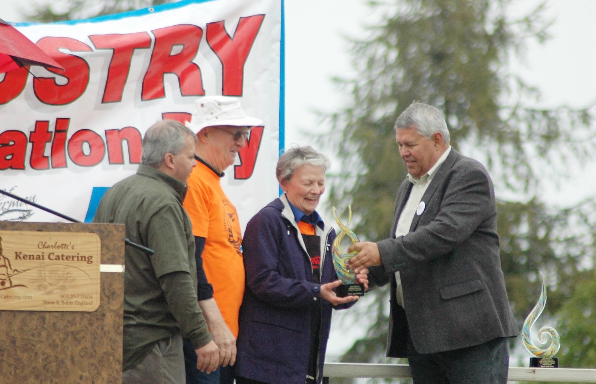 Borough Mayor Charlie Pierce (right) and Tim Navarre (far left) present an award to Will and Jane Madison for their work on the annual Industry Appreciation Day event on Saturday, Aug. 25, 2018 in Kenai, Alaska. (Photo by Elizabeth Earl/Peninsula Clarion)