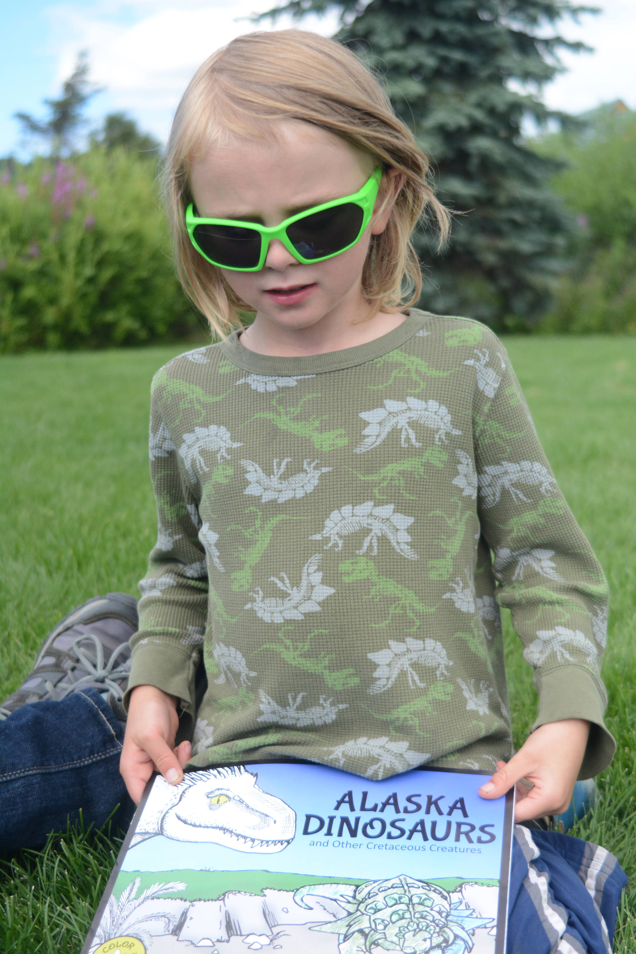 Silas Reising, 4, holds “Alaska’s Dinosaurs and Other Cretaceous Creatures,” a book written by his grandmother, Janet Klein, and mother, Deborah Klein, at Bishop’s Beach, Homer, Alaska, on Aug. 9, 2018. Not shown is Kai Reising, 6. Sylas and his older brother Kai were the inspiration for the Klein’s “color and learn” book. (Photo by Michael Armstrong/Homer News)