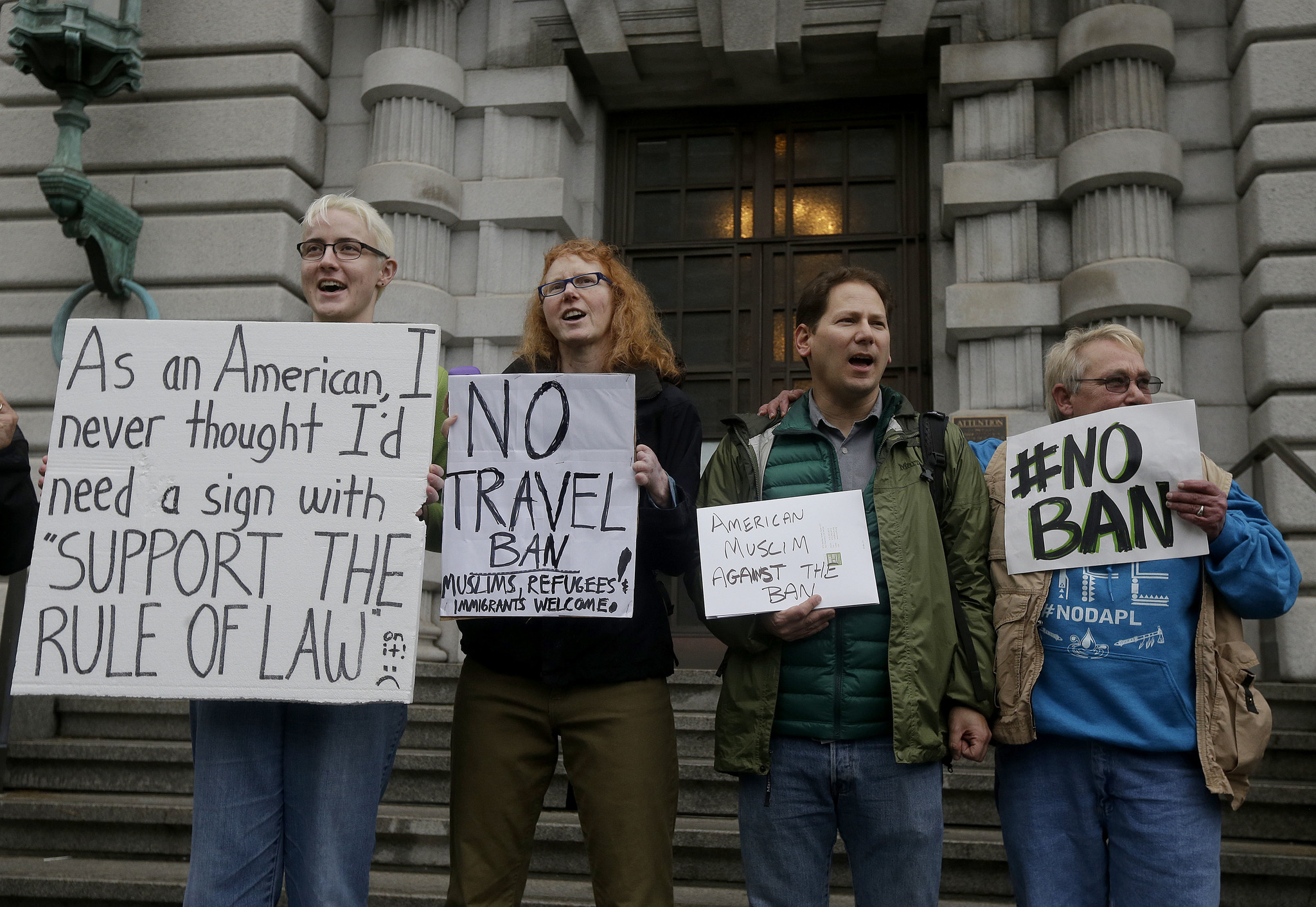 Kay Aull, from left, holds a sign and chants with Beth Kohn, Paul Paz y Mino and Karen Shore outside of the 9th U.S. Circuit Court of Appeals in San Francisco, Tuesday, Feb. 7, 2017. President Donald Trump’s travel ban faced its biggest legal test yet Tuesday as a panel of federal judges prepared to hear arguments from the administration and its opponents about two fundamentally divergent views of the executive branch and the court system. (AP Photo/Jeff Chiu)