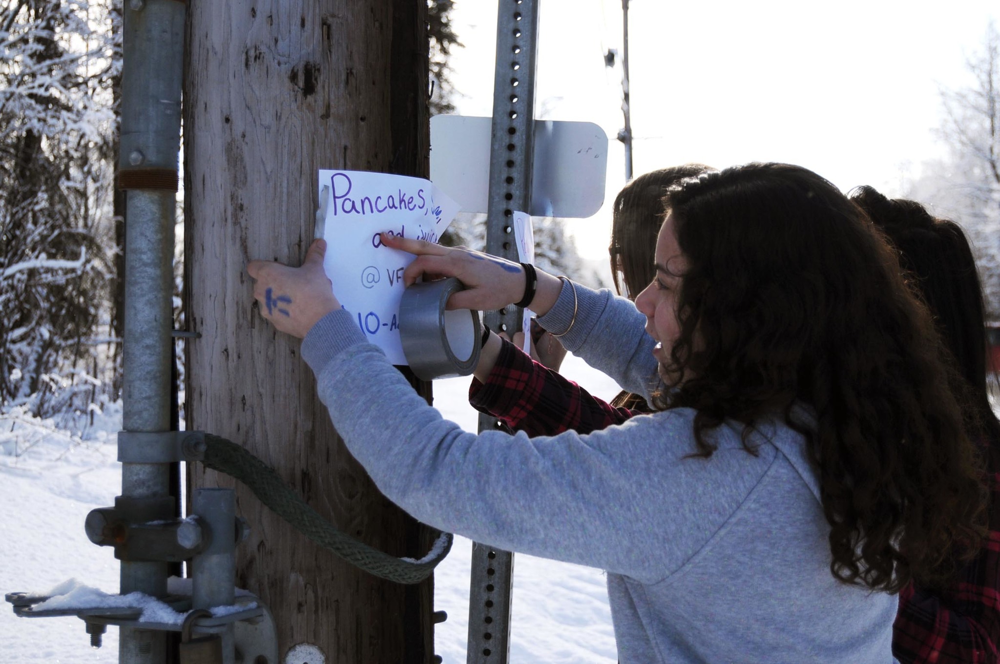 Tatihana DeHoyos, an eighth-grader at Skyview Middle School, tapes up a flyer with assistance from Kendra Rolence (far left) and Priscila Moreno (center), both seventh-graders at Skyview Middle School, to promote a pancake breakfast fundraiser for a school trip on Sunday, Feb. 19, 2017, in Soldotna, Alaska. DeHoyos and other eighth-graders from the middle school will travel to Washington, D.C., Williamsburg, Virginia, and New York City to visit museums and monuments and take in a Broadway show during the last week of May. They held a pancake breakfast at the Veterans of Foreign Wars post in Soldotna on Sunday from 12p.m. &