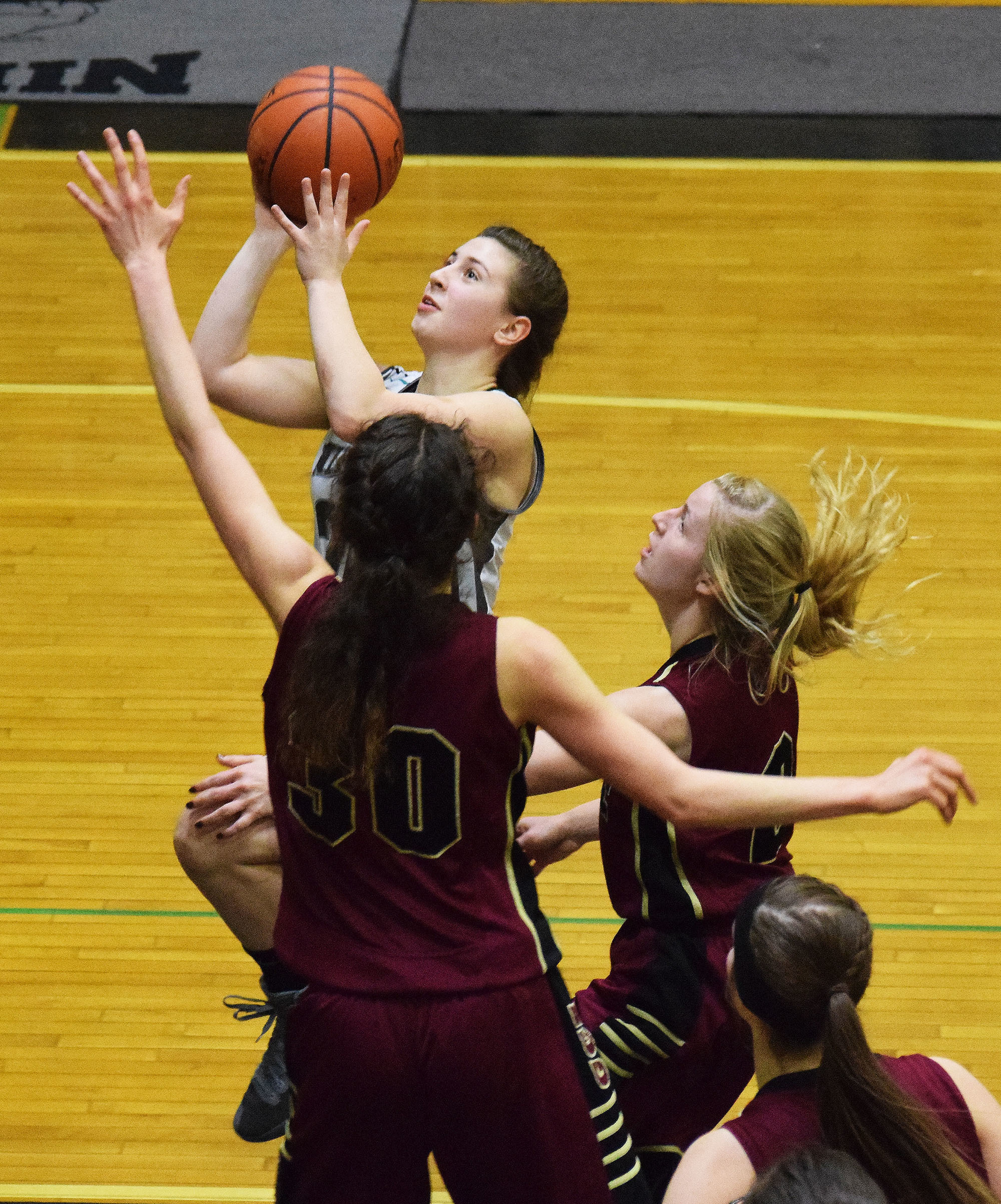 Nikiski’s Kelsey Clark looks to the rim against Grace Christian defenders Sarah Laker (30) and Annie VanderWeide, Friday at Nikiski High School. (Photo by Joey Klecka/Peninsula Clarion)