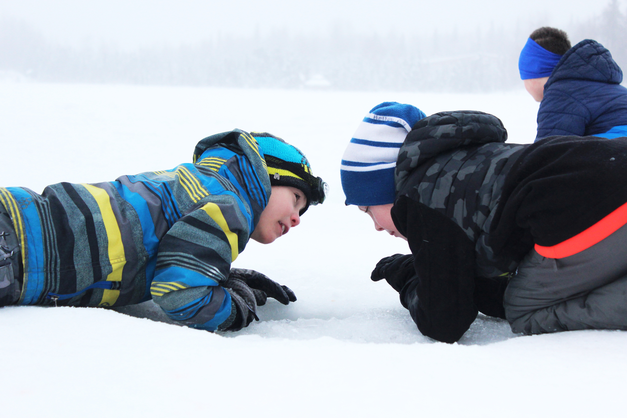 Third grader Ryder Lagerson, left, uses his headlight to help his Kaleidoscope School of Arts and Sciences classmate and Josiah Holloway, right, try to catch a fish during an ice fishing outing Friday, Feb. 24, 2017 at Sport Lake in Soldotna, Alaska. Hundreds of students from multiple Kenai Peninsula School District schools take part in the Alaska Department of Fish and Game's "Salmon in the Classroom" program each year, which includes three ice fishing outings in the winter. (Megan Pacer/Peninsula Clarion)