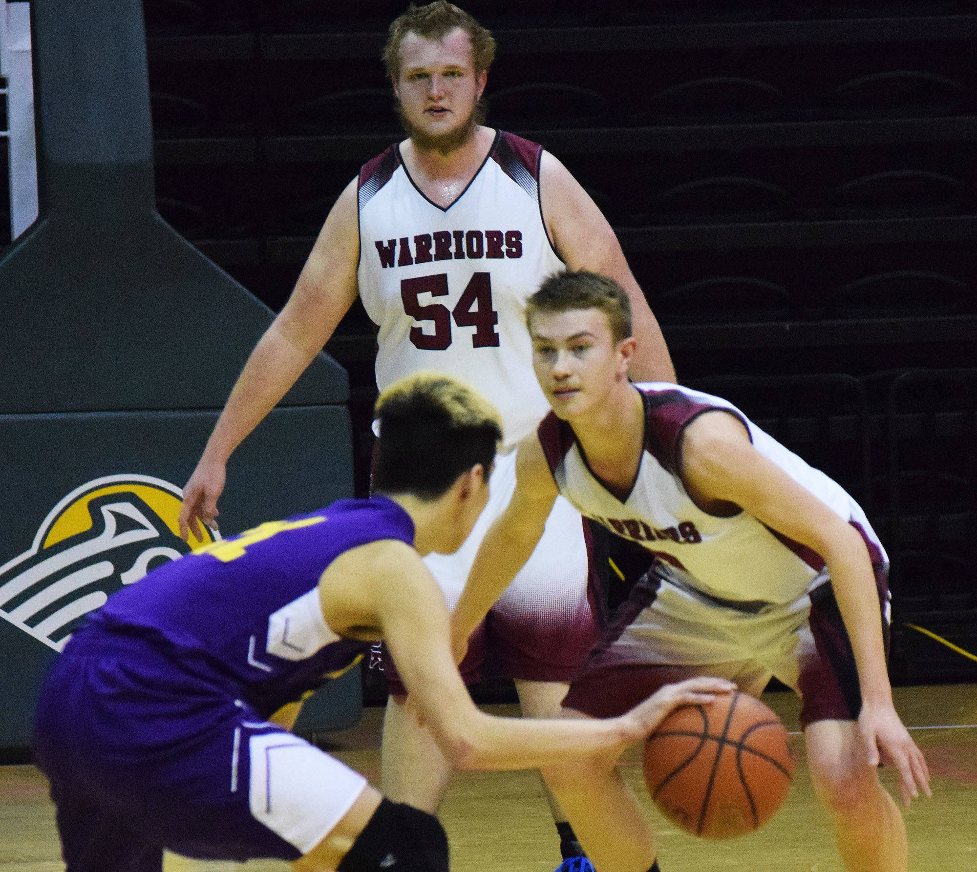Nikolaevsk’s Anfim Kalugin (54) looks on as Warriors teammate Kalenik Molodih guards Hydaburg’s Roger Trout, Friday, March 17, 2017, at the Class 1A state tournament held at the Alaska Airlines Center in Anchorage. (Photo by Joey Klecka/Peninsula Clarion)
