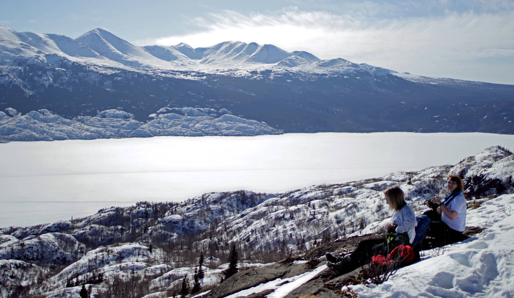 Kat Sorensen (left) and Elizabeth Earl rest on a snow-free patch of rock overlooking Skilak Lake on March 18 in the Kenai National Wildlife Refuge. (Ben Boettger/Peninsula Clarion)