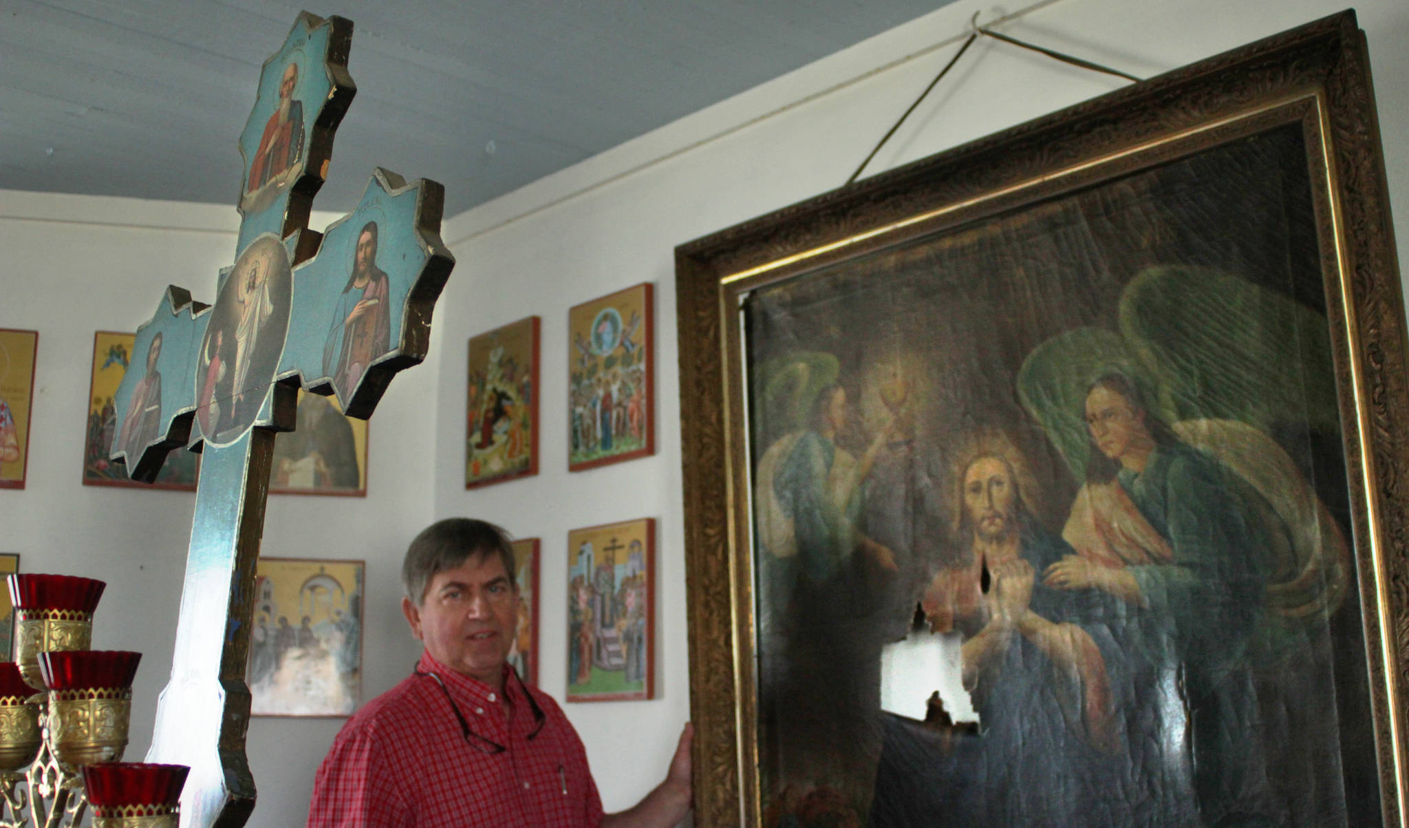 John Michael, a member of Kenai’s Holy Assumption of the Virgin Mary Russian Orthodox Church, prepares to carry a damaged icon of Jesus praying in the Garden of Gethsemane from the church’s sanctuary on Monday, May 15 in Kenai. In the foreground stands the wooden cross that fell backward during the January 2016 Iniskin Earthquake, tearing the icon’s canvas. After planning and fundraising for the icon’s repair since mid-2016, the church shipped it to an art restorer on Monday.