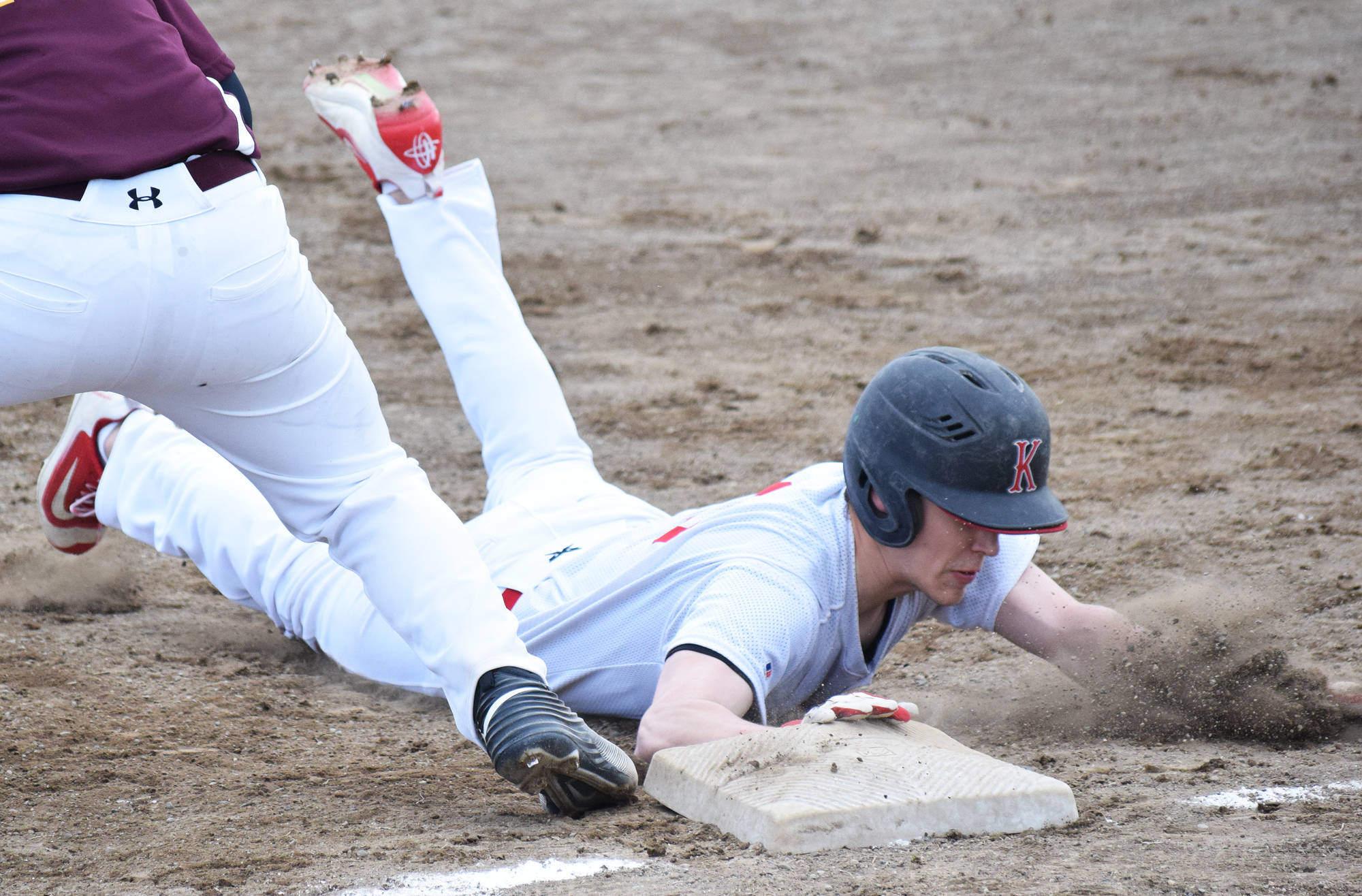 Kenai Central’s Ryan Johnson tags up to first base under Grace Christian’s Steven Brown, Friday evening at the Kenai Little League Fields. (Photo by Joey Klecka/Peninsula Clarion)