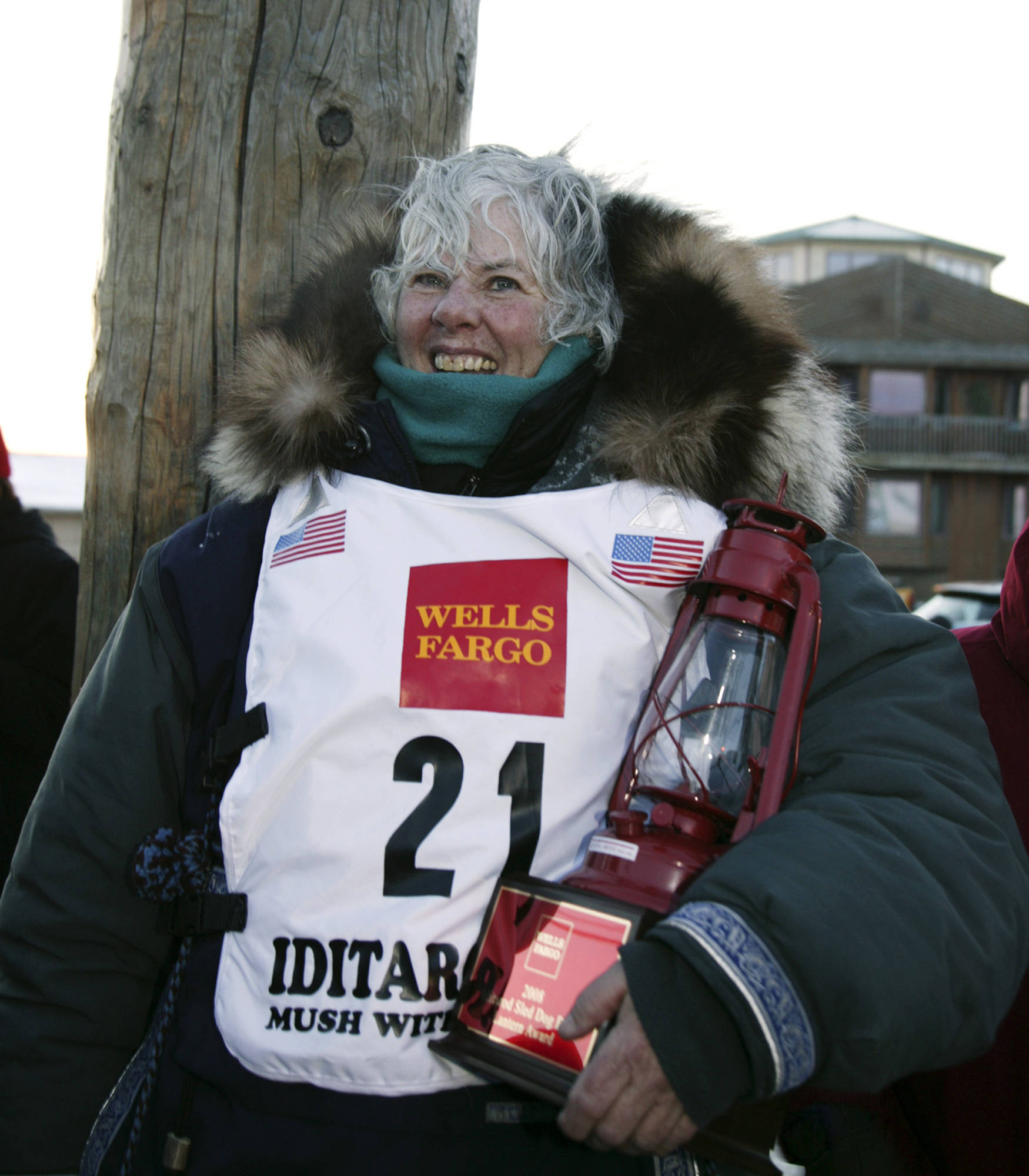 FILE - This March 17, 2008, file photo, shows Deborah Bicknell from Juneau, Alaska wearing a Wells Fargo bib and posing with the “Widow’s Lamp” which is lit at the beginning of the Iditarod Trail Sled Dog Race and is blown out by the last musher to the end of the sled dog race in Nome, Alaska, signifying that the race is over. Wells Fargo has dropped its sponsorship of the world’s most famous sled dog race, a move race officials have blamed on animal rights groups targeting corporate offices outside Alaska. (AP Photo/Peggy Fagerstrom, File)