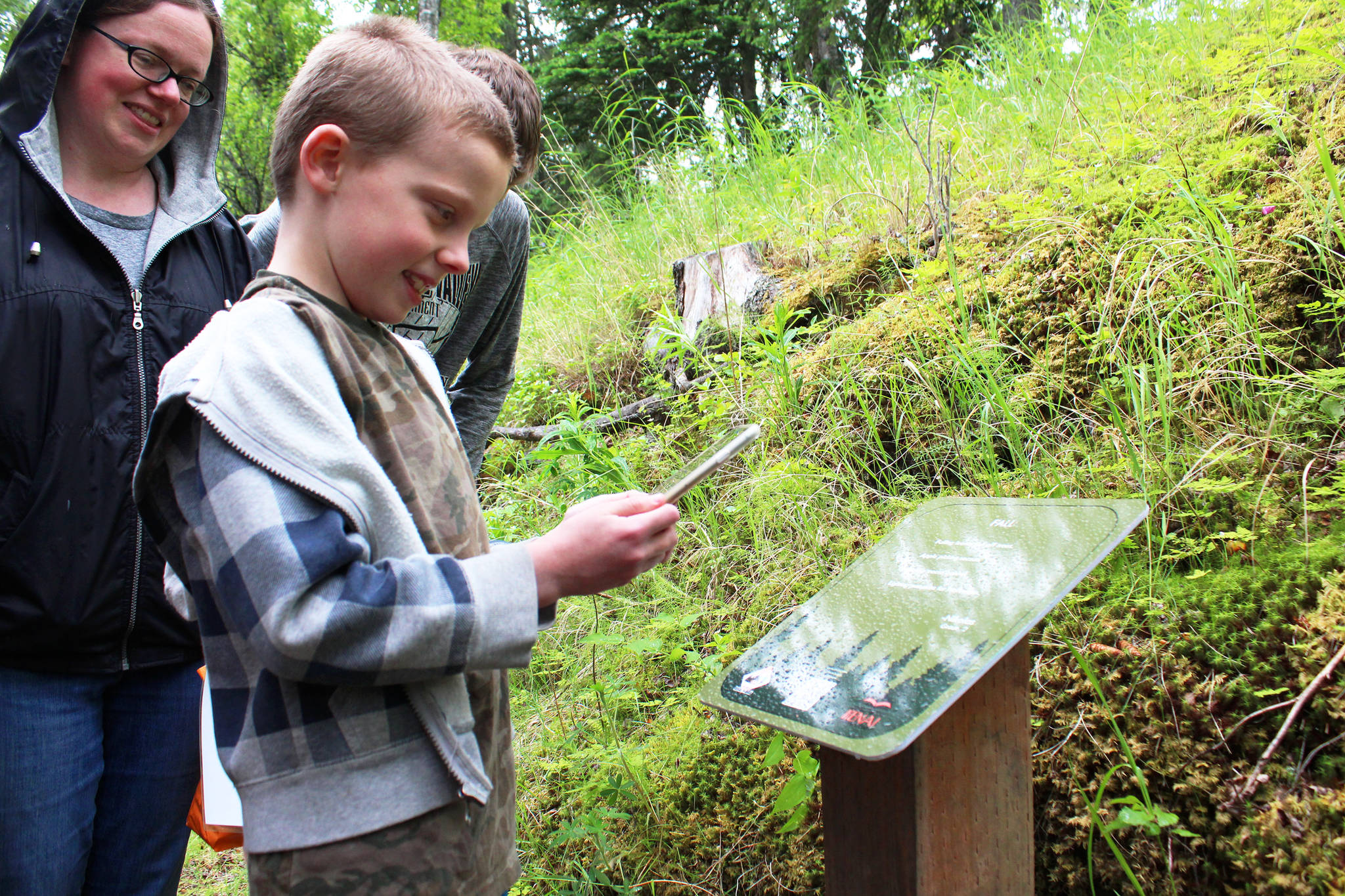 Nikolas Bezdecny scans a code on a sign displaying the poem he wrote for Pathways of Poetry on Saturday, July 1, 2017 on the trail at Kenai Municipal Park in Kenai, Alaska. Bezdecny is one of 12 students chosen as winners of the contest out of 86 participants who wrote poems about nature from the project. Scanning the code on the signs brings up an audio recording of the authors reading their pieces. (Photo by Megan Pacer/Peninsula Clarion)