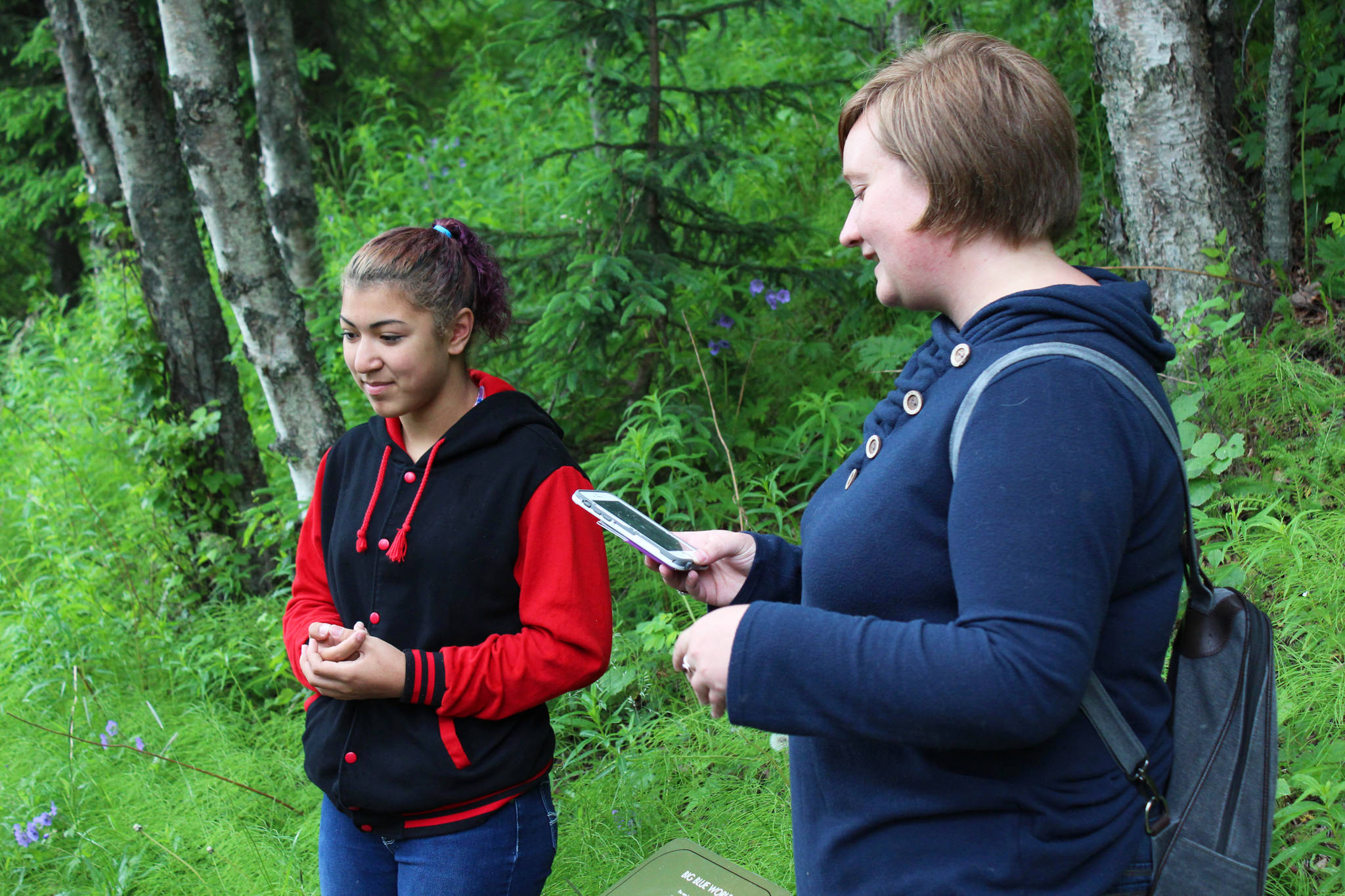 Ryanna Thurman, right, finishes listening to an oration of Kenai Central High School student Kassandra Renfrow’s poem, one of the winning entries to the Pathways of Poetry contest, Saturday, July 1, 2017 on the trail at Kenai Municipal Park in Kenai, Alaska. A panel of judges chose 12 winners out of 86 student participants, whose poems about nature are placed on signs along the trail. Scanning the codes on the signs brings up a recording of the authors reading their pieces. (Photo by Megan Pacer/Peninsula Clarion)