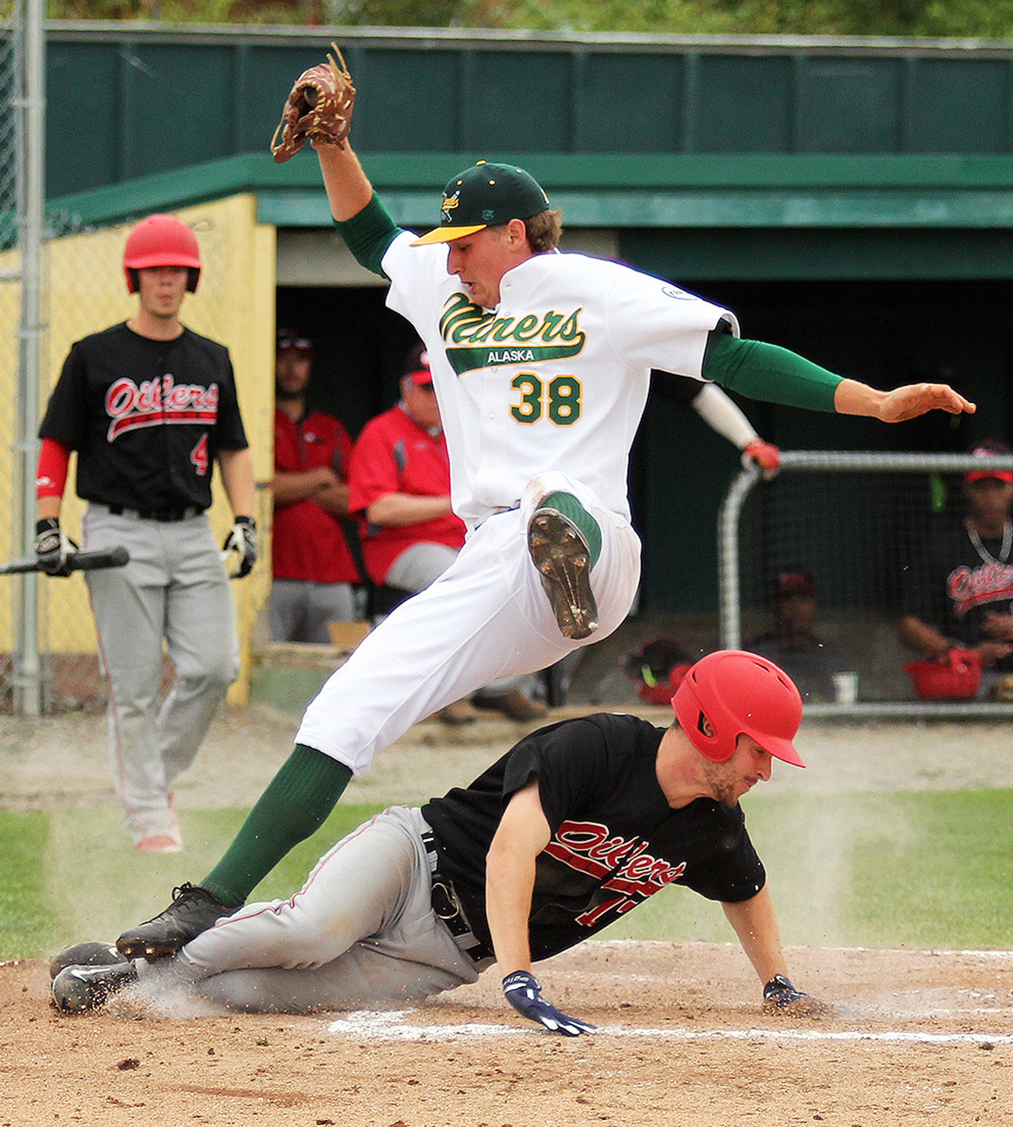 Mat-Su pitcher John Doxakis falls over Peninsula Oilers outfielder Thomas Ruddy after Doxakis reached up to snag a high throw as Ruddy slides into home to score the go-ahead run during a 2-1 victory over the Miners Friday at Hermon Brothers Field in Palmer. (Photo by Jeremiah Bartz/Frontiersman)