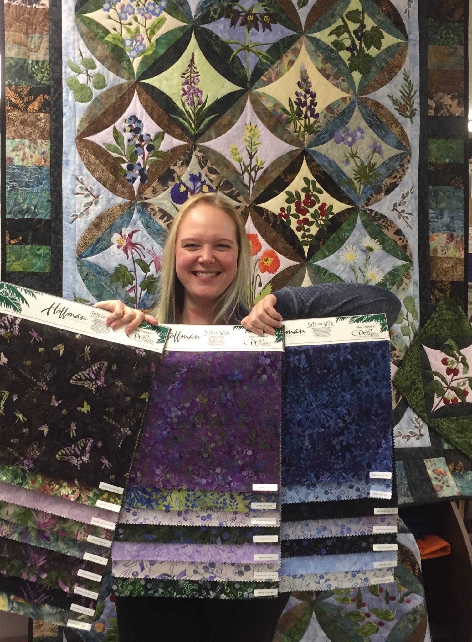 Dana Woodard holds up a selection of her newly designed fabric collection in front of a quilted pattern on display, and for sale, at Kenai Fabric Center. (Photo courtesy Gwen Woodard)