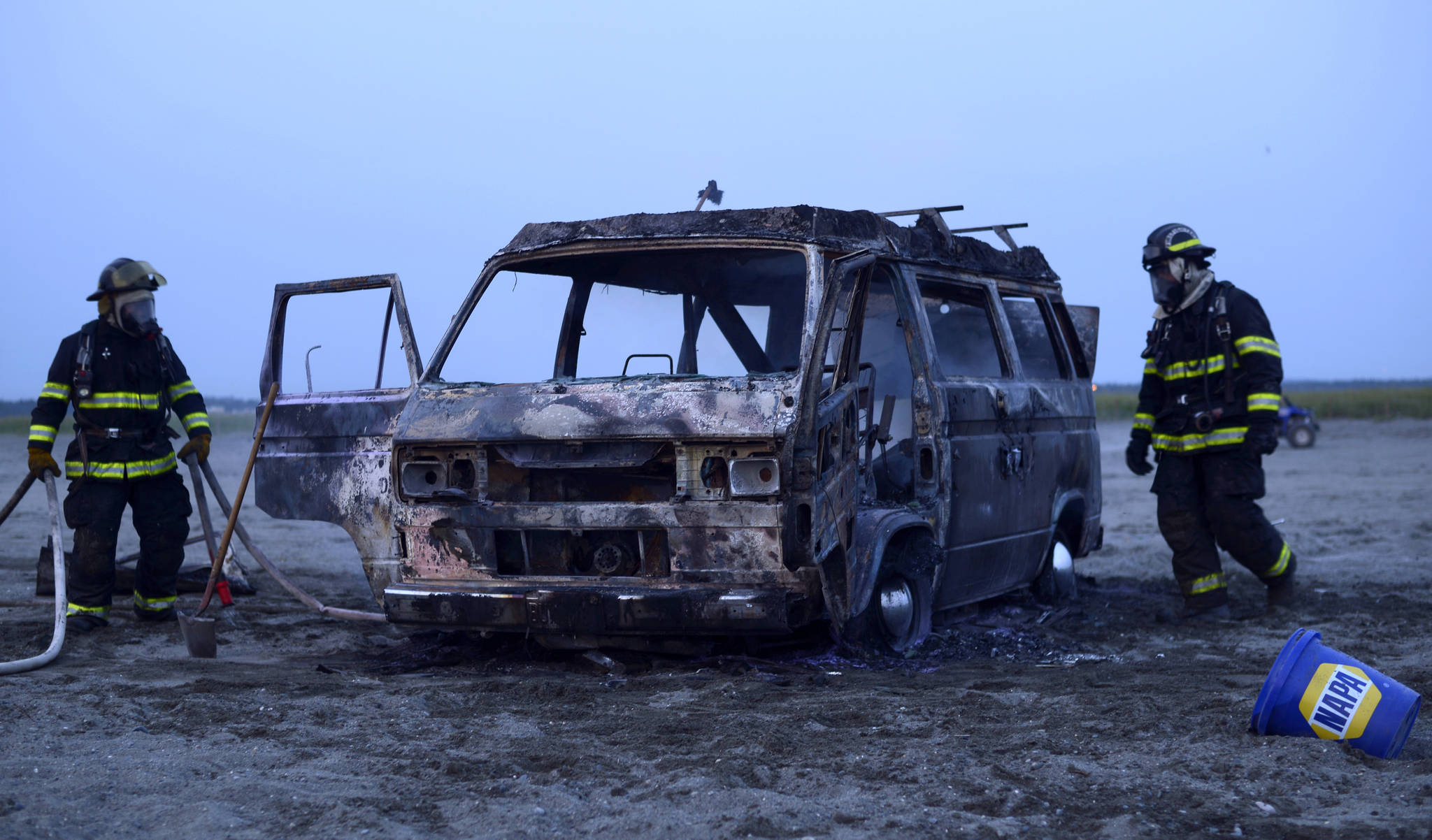 Two Kenai firefighters clean up a 1987 Volkswagen Westfallia camper van that caught fire Thursday, July 13, 2017 on the south beach in Kenai, Alaska. No one was in the van when it burnt, and there were no injuries. (Photo by Ben Boettger/Peninsula Clarion)