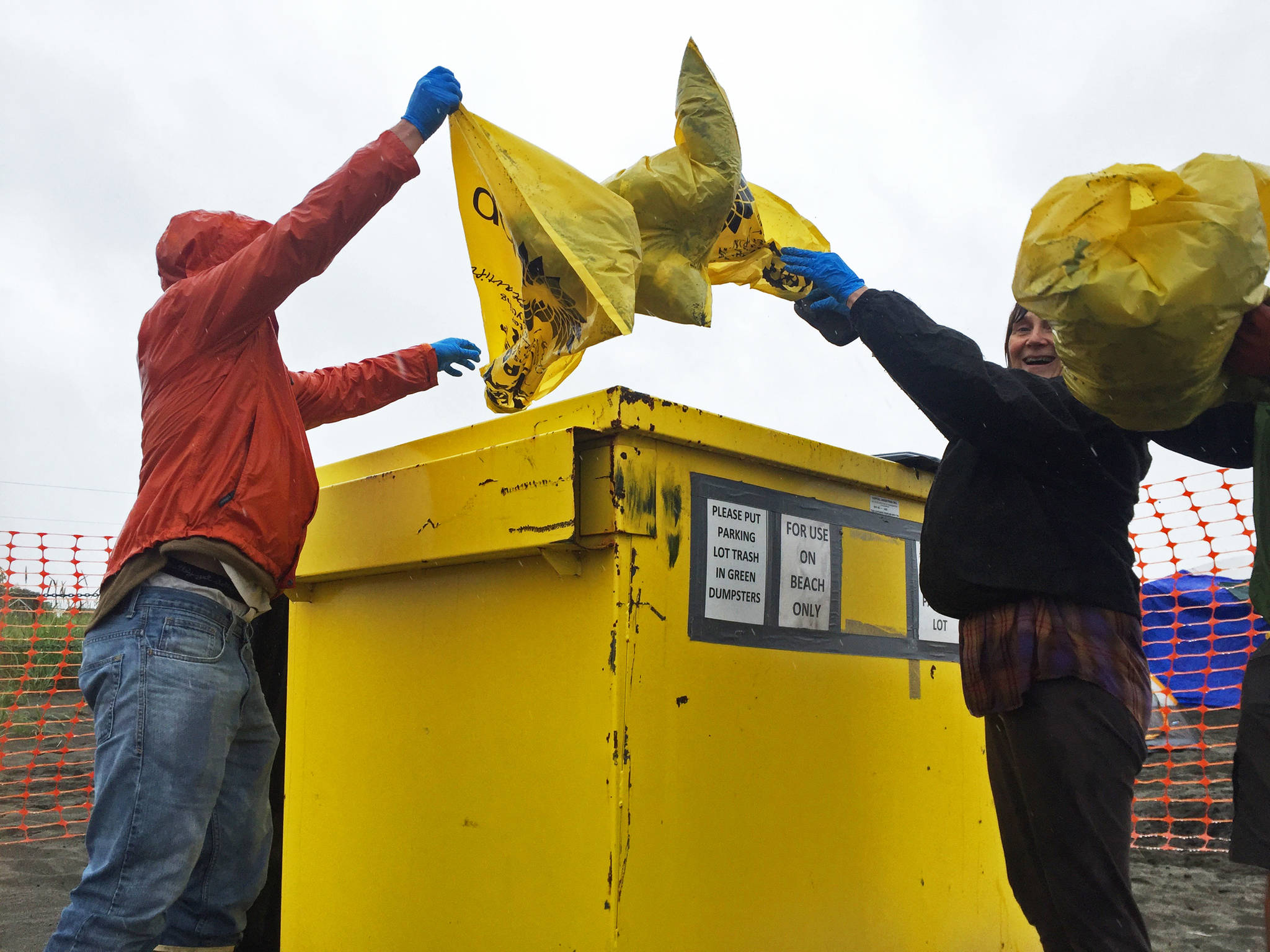 Karl Danielson (left), a senior at Kenai Central High School and a member of the KCHS Cross Country Ski Team, his mom Teresa Danielson (center) and coach Brad Nyquist (right) empty out their garbage bags into a bin at the north Kenai Beach on Tuesday, July 18, 2017 in Kenai, Alaska. Members of the ski team helped clean up the beach Tuesday as a fundraiser for the team’s activities. (Photo by Elizabeth Earl/Peninsula Clarion)