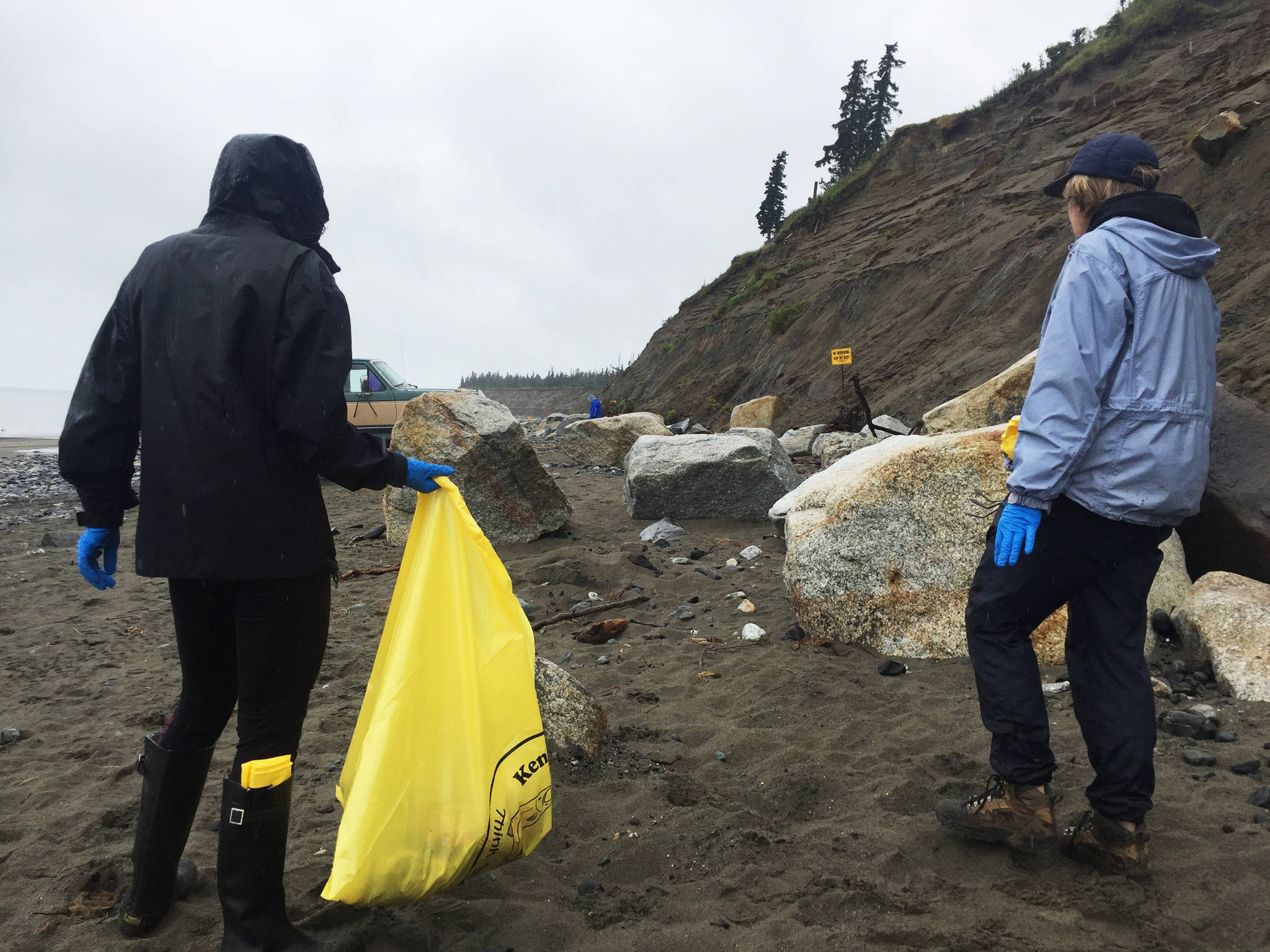 Theresa Salzetti (left) and Chris Bergholtz (right), a coach on the Kenai Central High School Cross Country Ski Team, head down the beach to clean up garbage left by personal-use dipnetters on the north Kenai Beach on Tuesday, July 18, 2017 in Kenai, Alaska. Members of the ski team helped clean up the beach Tuesday as a fundraiser for the team’s activities. (Photo by Elizabeth Earl/Peninsula Clarion)