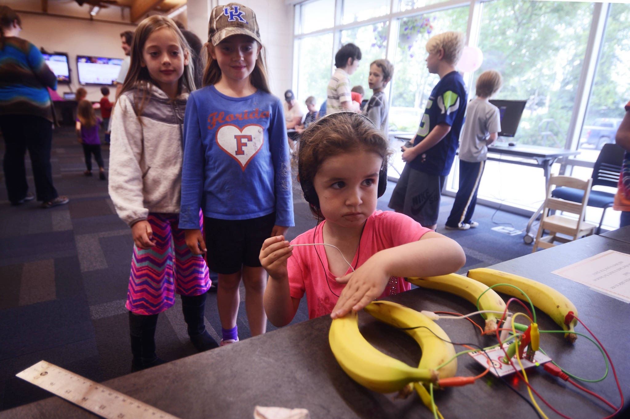 Tayla Cole plays with a program called “Banana Piano,” running on a Raspberry Pi computer, as Taylor Crista (right) and Amy Sevast look on during a Raspberry Pi demonstration on Monday, July 24, 2017 at the Kenai Public Library in Kenai, Alaska. The program uses the fruit’s electrical conductivity, and the conductivity of human skin, to make bannas — wired through an input device called Makey Makey — produce digital tones when touched. Kenai Library intern Kianna Steadman used the Bannana Piano and other inventions to introduce the Kenai Library’s twelve Raspberry Pi computers, which will be the subject of three workshops at the library next week, and a club that will meet weekly thereafter. (Photo by Ben Boettger/Peninsula Clarion)