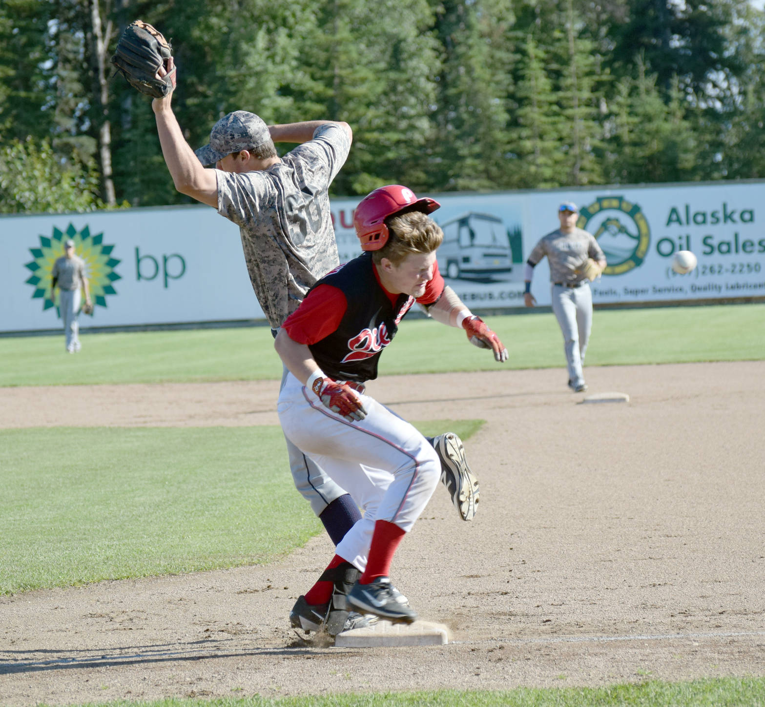 Kellen Strahm beats out a single in the bottom of the first inning as the ball gets away from Chugiak-Eagle River Chinooks first baseman Luke Coffey on Thursday, July 27, 2017, at Coral Seymour Memorial Park in Kenai. (Photo by Jeff Helminiak/Peninsula Clarion)