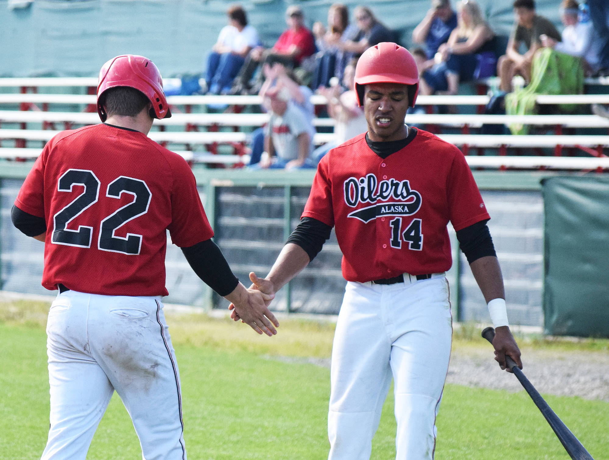 Isaac Deveaux (14) gives Peninsula Oilers teammate Kellen Strahm a low five after Strahm scored a run against the Chugiak Chinooks, Saturday afternoon at Coral Seymour Memorial Ballpark in Kenai. (Photo by Joey Klecka/Peninsula Clarion)