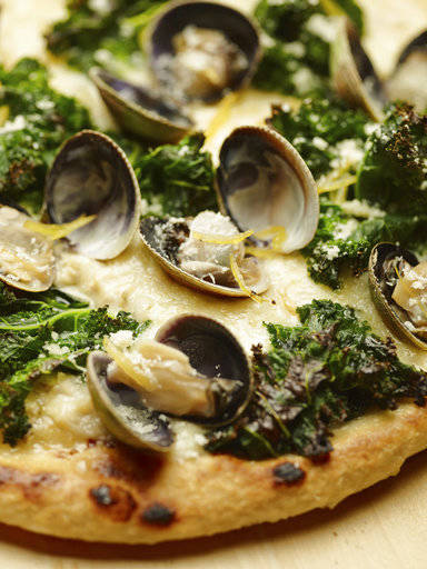This June 2 photo provided by The Culinary Institute of America shows a grilled white pizza with cockles, lemon and kale. This dish is from a recipe by the CIA. (Phil Mansfield/The Culinary Institute of America via AP)