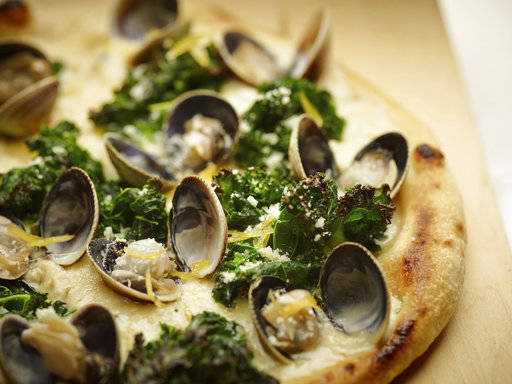 This June 2 photo provided by The Culinary Institute of America shows a grilled white pizza with cockles, lemon and kale. This dish is from a recipe by the CIA. (Phil Mansfield/The Culinary Institute of America via AP)