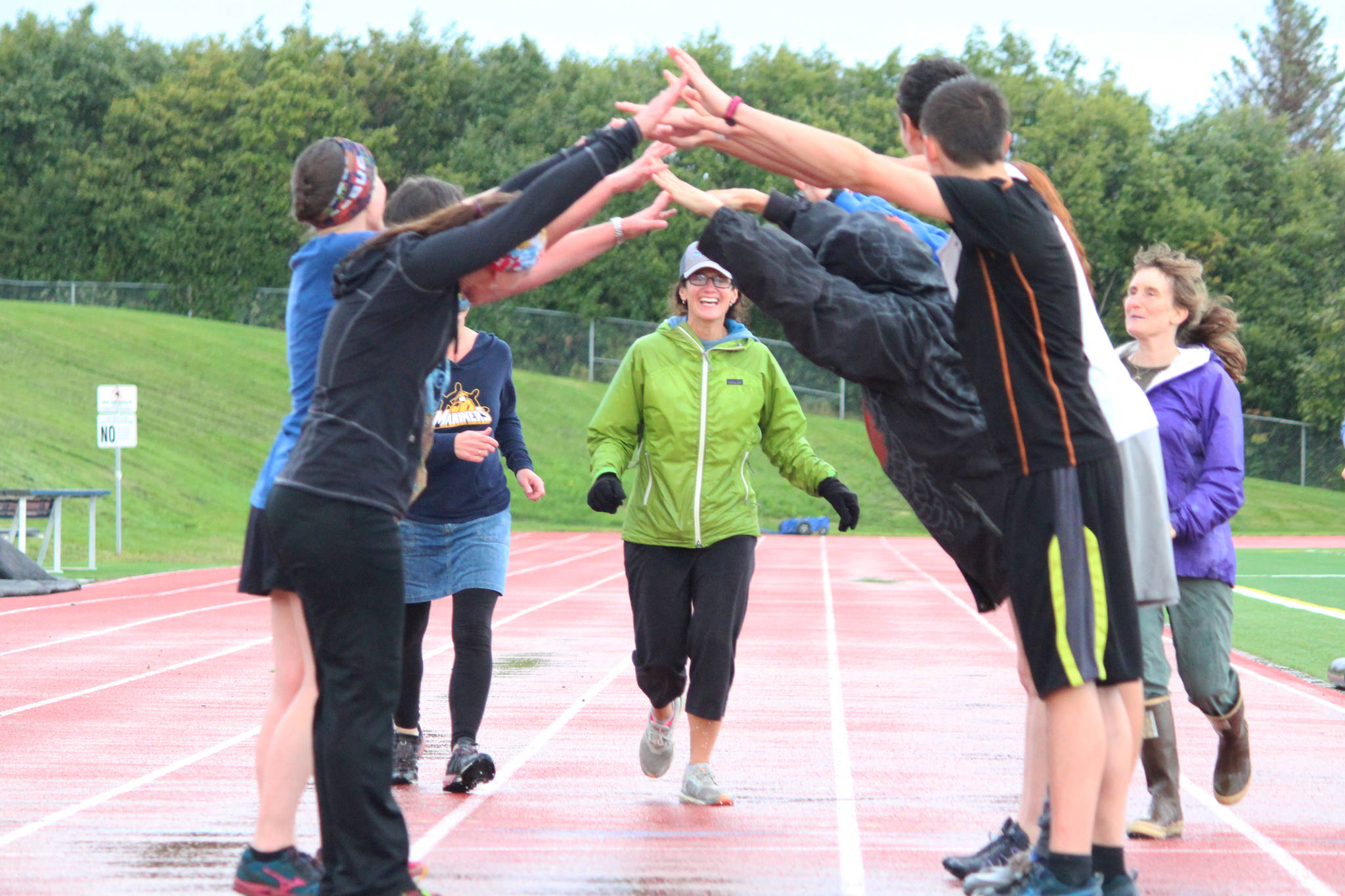 Saundra Hudson, an active member of and advocator for the Homer running community and teacher at Homer High School, runs under a human bridge during the Mariner Mile event Thursday, Sept. 14, 2017 at the high school track in Homer, Alaska. Hudson experienced a head injury when she slipped on the ice running this past March, and Thursday’s fundraising event for the Kachemak Bay Running Club was the first time she’s run in six months. (Photo by Megan Pacer/Homer News)
