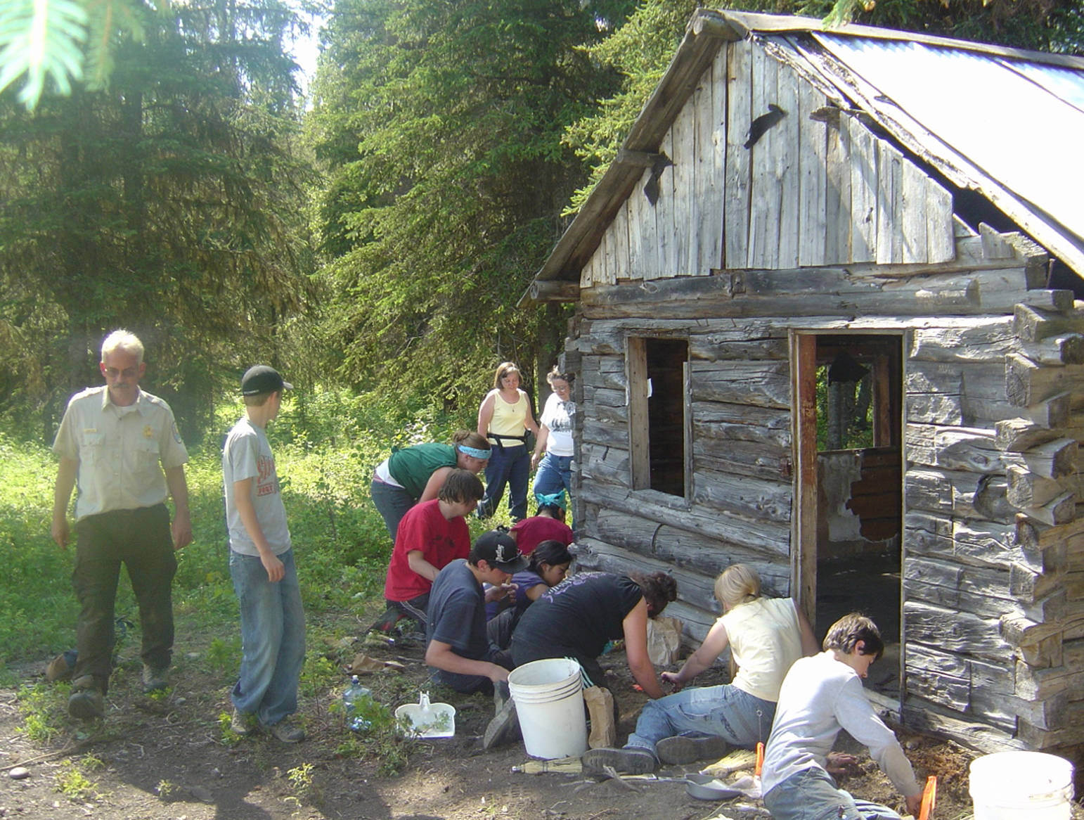 Kids from the Kenaitze Indian Tribe Susten Archaeology Camp excavate around a historical cabin in preparation for it be moved by Gary Titus from the Kenai National Wildlife Refuge. (Photo provided)