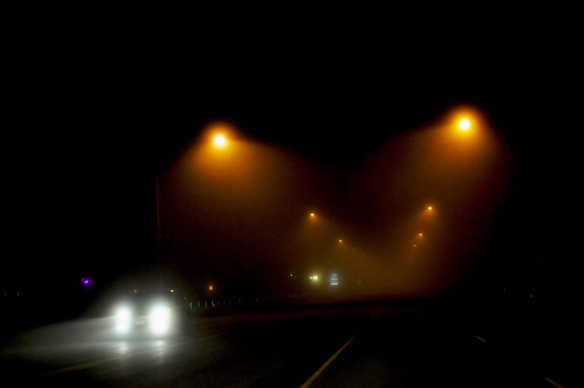 A car crosses the David E. Douthit Veterans Memorial Bridge over the Kenai River through dense fog on Tuesday, Oct. 31, 2017 in Soldotna, Alaska. A heavy fog rolled over the western Kenai Peninsula Tuesday evening, resulting in cancelled flights in and out of the Kenai Municipal Airport and ensconcing Halloween trick-or-treaters in an eerie mist colored orange or white by the streetlamps. By morning, the fog had thinned and the temperature dropped to the high 20s, with some fog predicted to continue in the morning and evening through Wednesday and Thursday, according to the National Weather Service. (Photo by Elizabeth Earl/Peninsula Clarion)