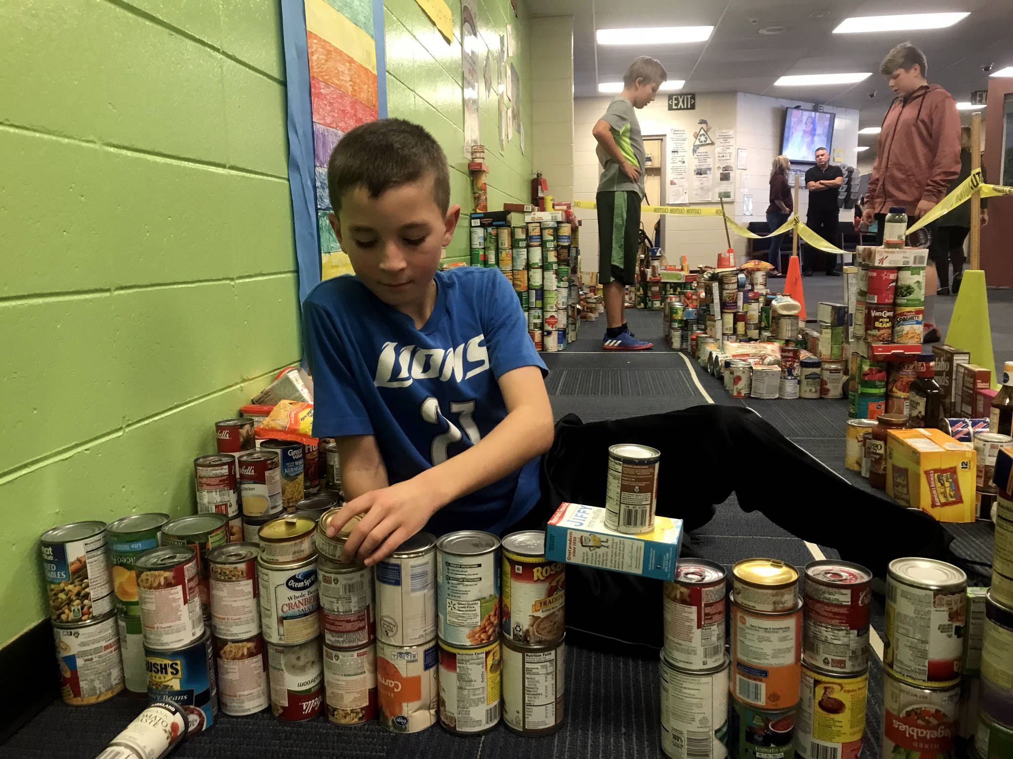 Zac Buckbee works on the ‘canstruction’ of Puncity while classmates visit the small city, made of donated food in the hallways of Redoubt Elementary School in Soldotna on Thursday. (Photo by Kat Sorensen/Peninsula Clarion)