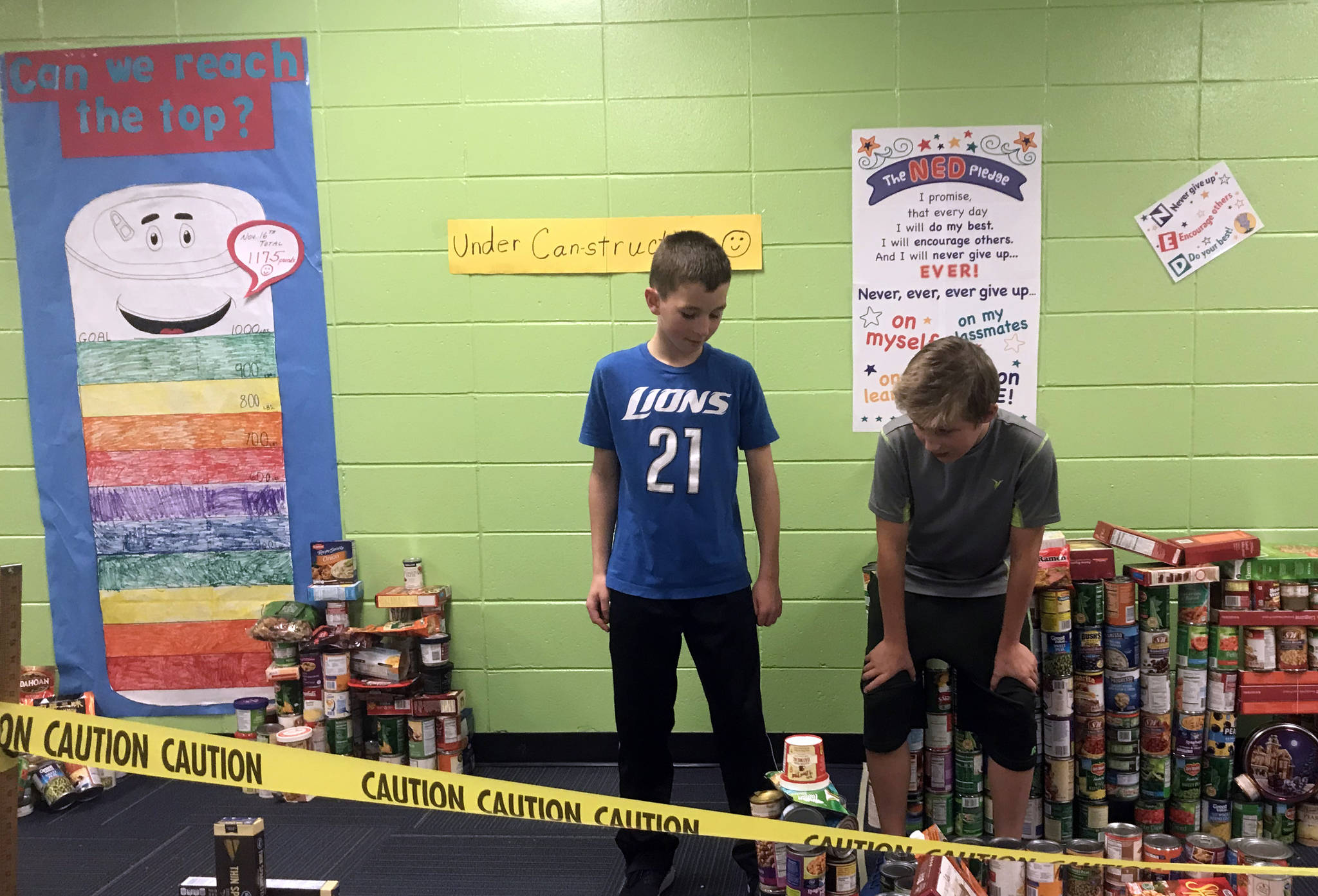 Zac Buckbee, left, and Jace O’Reagan stand amidst their ‘canstruction,’ Puncity, which they, along with Enoch Frederickson, built with over 1,000 pounds of donated food. (Photo by Kat Sorensen/Peninsula Clarion)