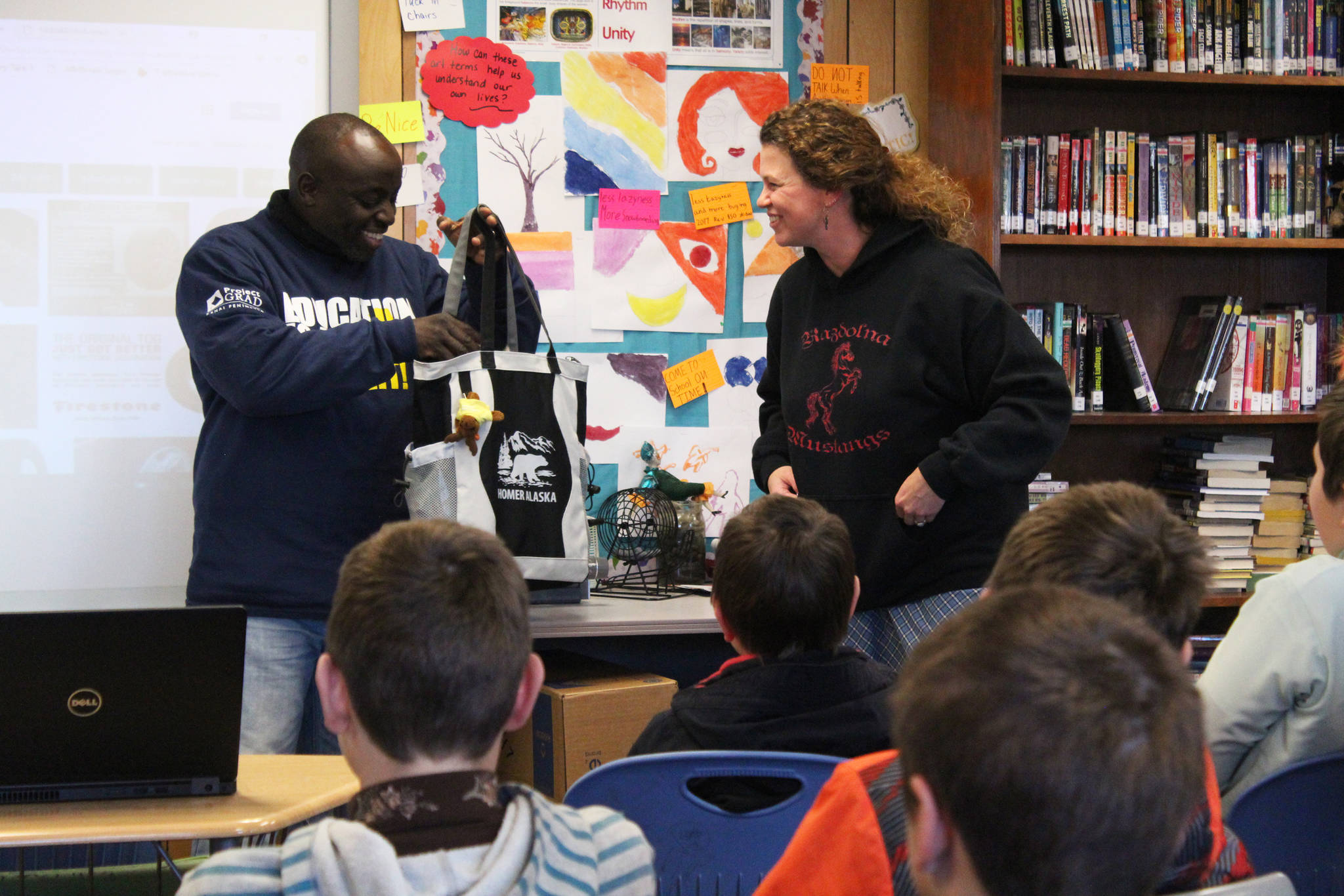 Laura Murphy, a teacher at Razdolna School, presents Chris Mburu, a human rights lawyer who works for the United Nations, with a care package full of Alaska-themed gifts during his presentation to the school Friday, Nov. 17, 2017 in Razdolna, Alaska. The students gifted Mburu and fellow presenter Kimani Nyambura, both from Kenya, several things from their area, including smoked salmon, the pelt of an ermine one of the students had trapped, and a pumpkin grown in one of the nearby high tunnels. (Photo by Megan Pacer/Homer News)