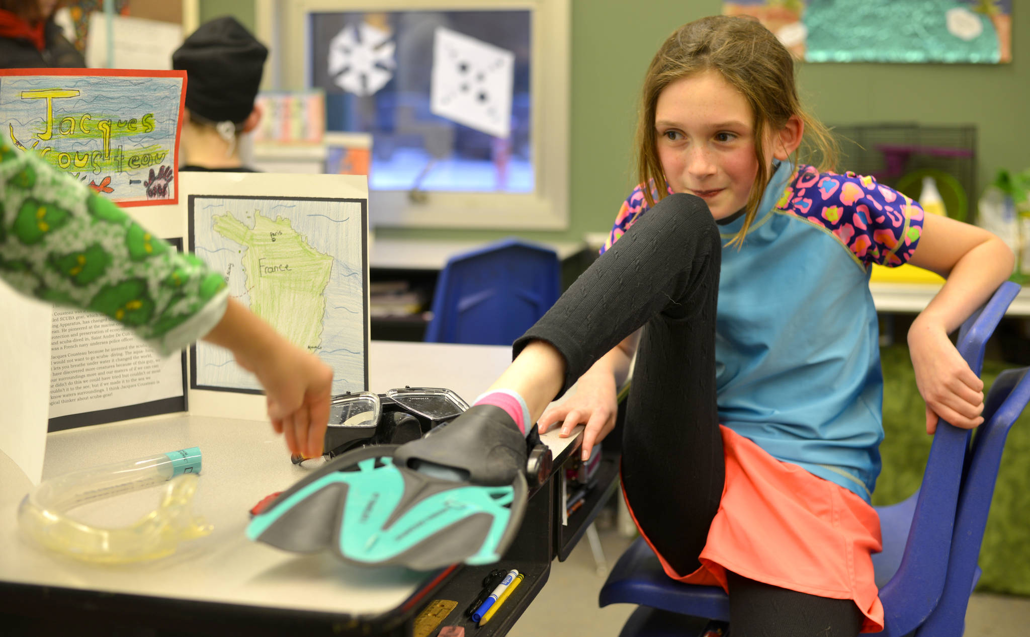 Kiya Hudson anticipates the pressing of her button during the Kaleidoscope School’s Wax Museum on Thursday, Dec. 7. 2017 in Kenai, Alaska, which tasked the fifth grade class with impersonating a notable historical figure and taking on their persona. When a visitor to the wax museum pushed a student’s button, they would recite their figure’s biographical information in first person. Hudson said she stepped into Jacques Cousteau’s flippers for the assignment because she wants to be a scuba diver when she grows up. (Photo by Kat Sorensen/Peninsula Clarion)