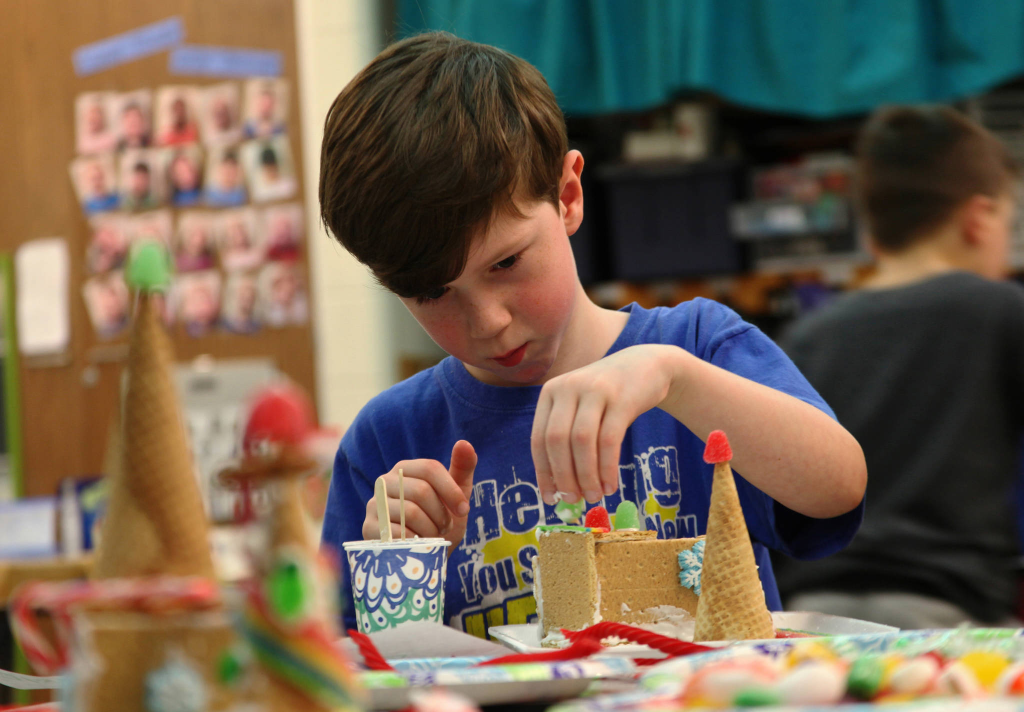 Gabriel Dravis sticks a gumdrop on to the gingerbread house he built from graham crackers, frosting, and candy in Stacy Tronnier’s first and second grade class at Kaleidoscope School of Arts and Science on Friday, Dec. 15 in Kenai, Alaska. Three first and second grade classes at Kaleido- scope made gingerbread houses on Friday to take home for display and/or eating. (Photo by Ben Boettger/Peninsula Clarion)