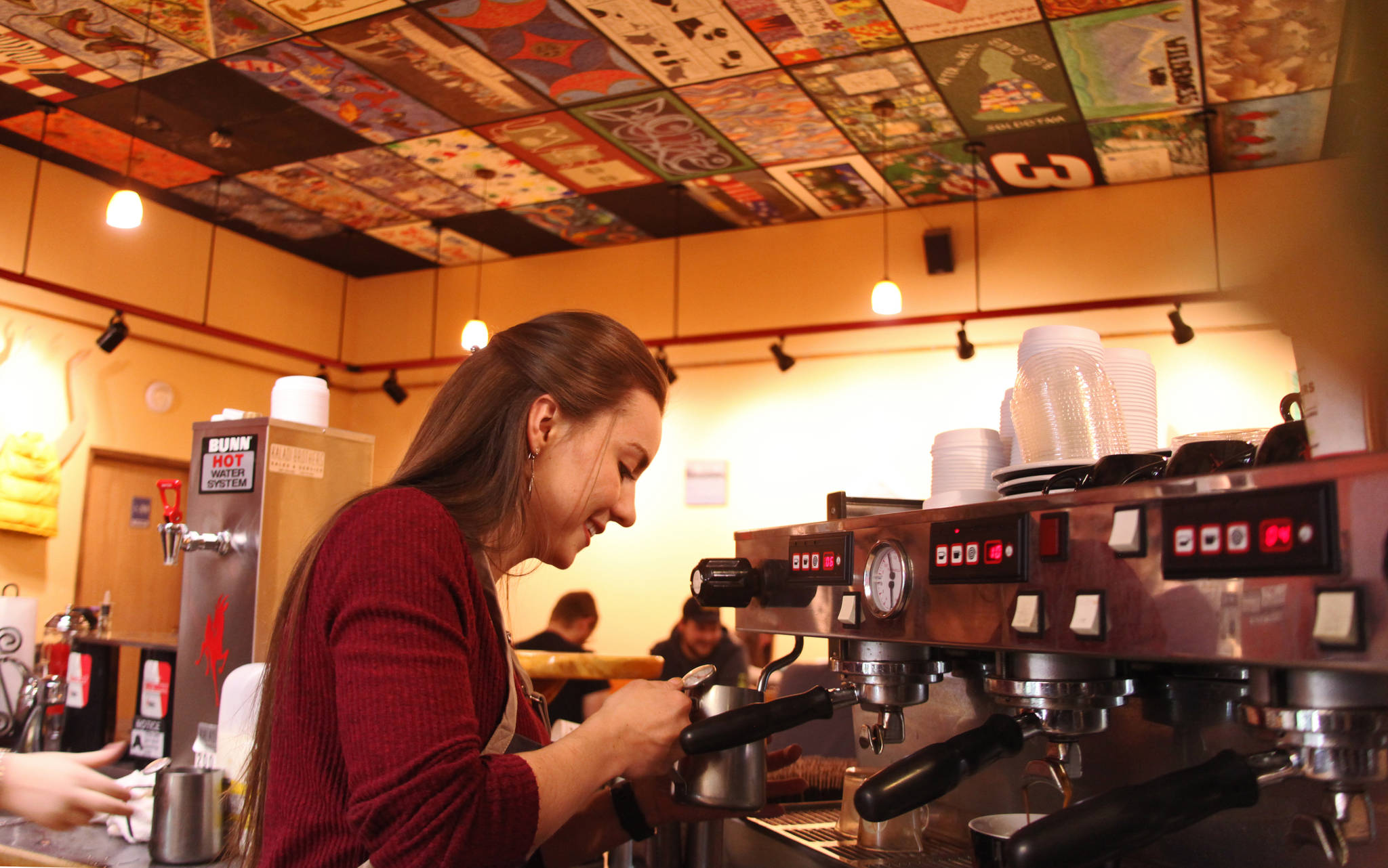 With the shop’s distinctive painted cieling panels above her, barrista Sarah Rawson steams milk to make a latte at Kaladi Brother’s Coffee during a busy evening on Saturday, Jan. 13 in Soldotna. Rawson and fellow barrista Hallie Riddall practiced latte art — creating designs by carefully and precisely pouring steamed milk into coffee — between serving customers Saturday evening. (Ben Boettger/Peninsula Clarion)